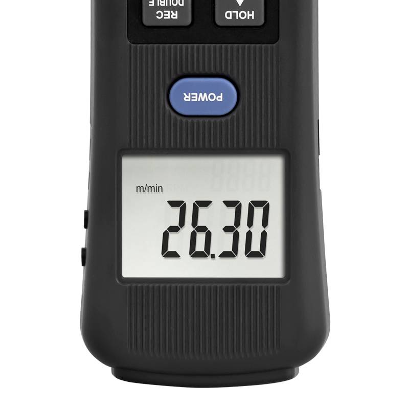 Cyfrowy anemometr wskazuje '26,30 m/min', średniej wielkości urządzenie z wyświetlaczem LCD i przyciskami do sterowania zasilaniem, zatrzymywaniem oraz jednostkami miary.