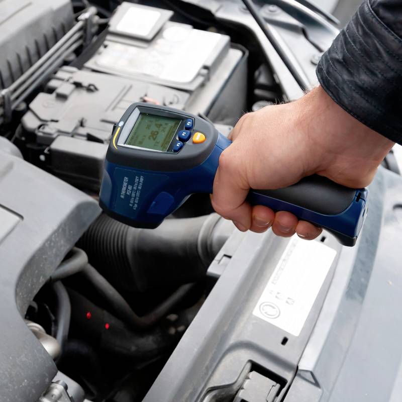 Osoba sprawdza silnik samochodu za pomocą termometru cyfrowego, aby zmierzyć temperaturę.