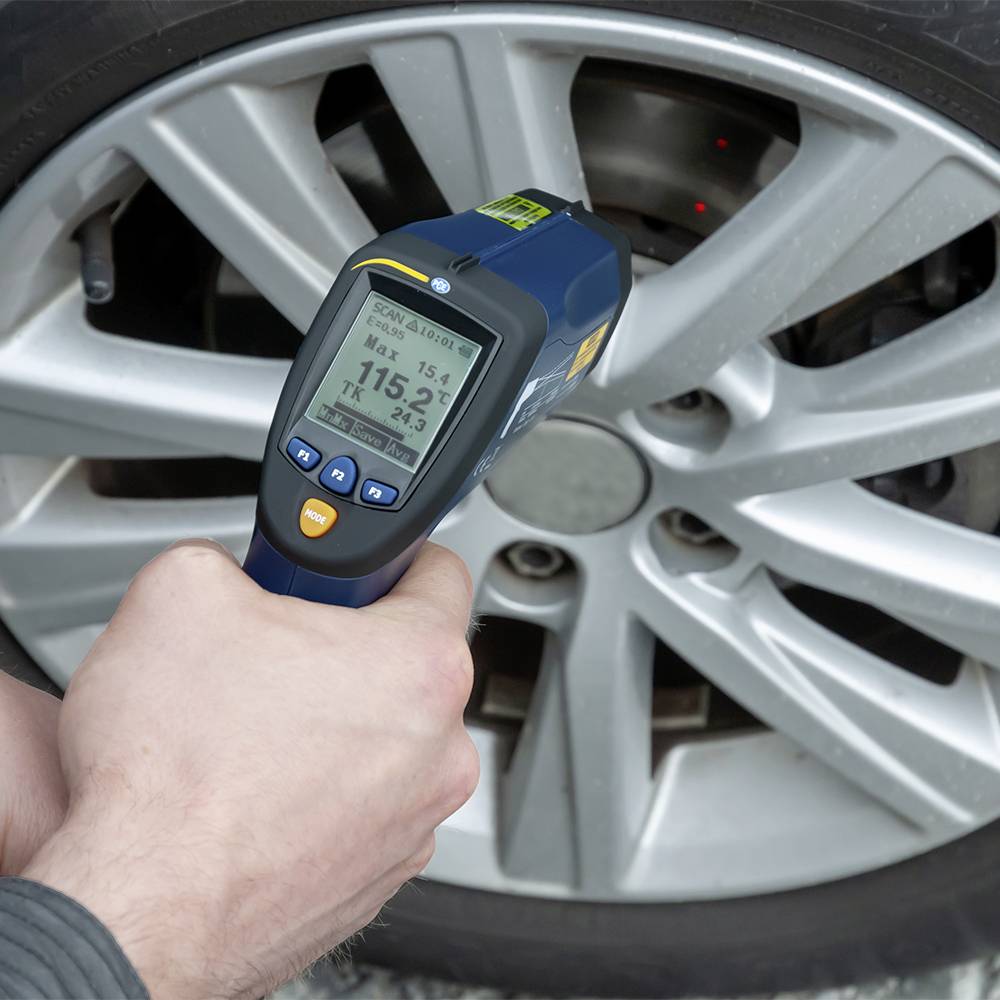 Osoba mierzy temperaturę opony samochodowej za pomocą termometru na podczerwień. Wyświetlacz wskazuje 115,2 stopni Fahrenheita.