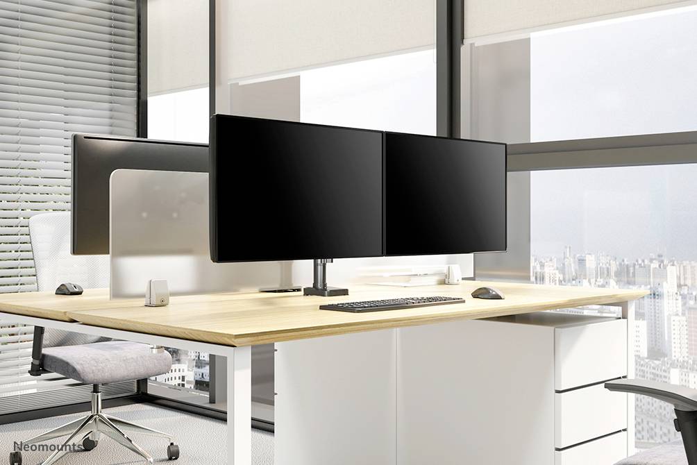 Nowoczesne biuro z dużym biurkiem, dwoma monitorami, klawiaturą, myszką i fotelem biurowym. Duże okna oferują widok na miasto.