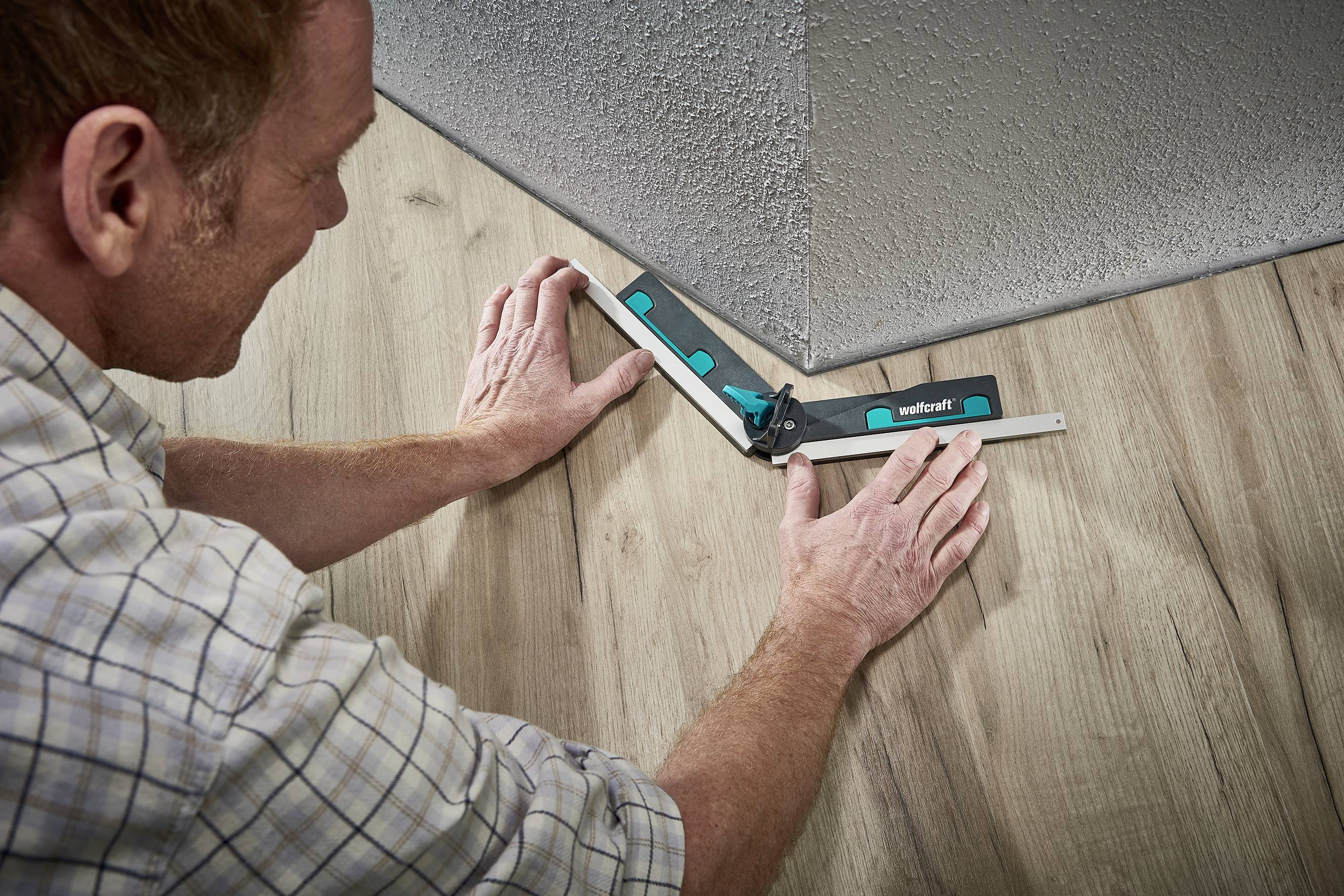 Mężczyzna mierzy kąt podłogi drewnianej kątomierzem, aby odpowiednio dobrać i przyciąć materiał.