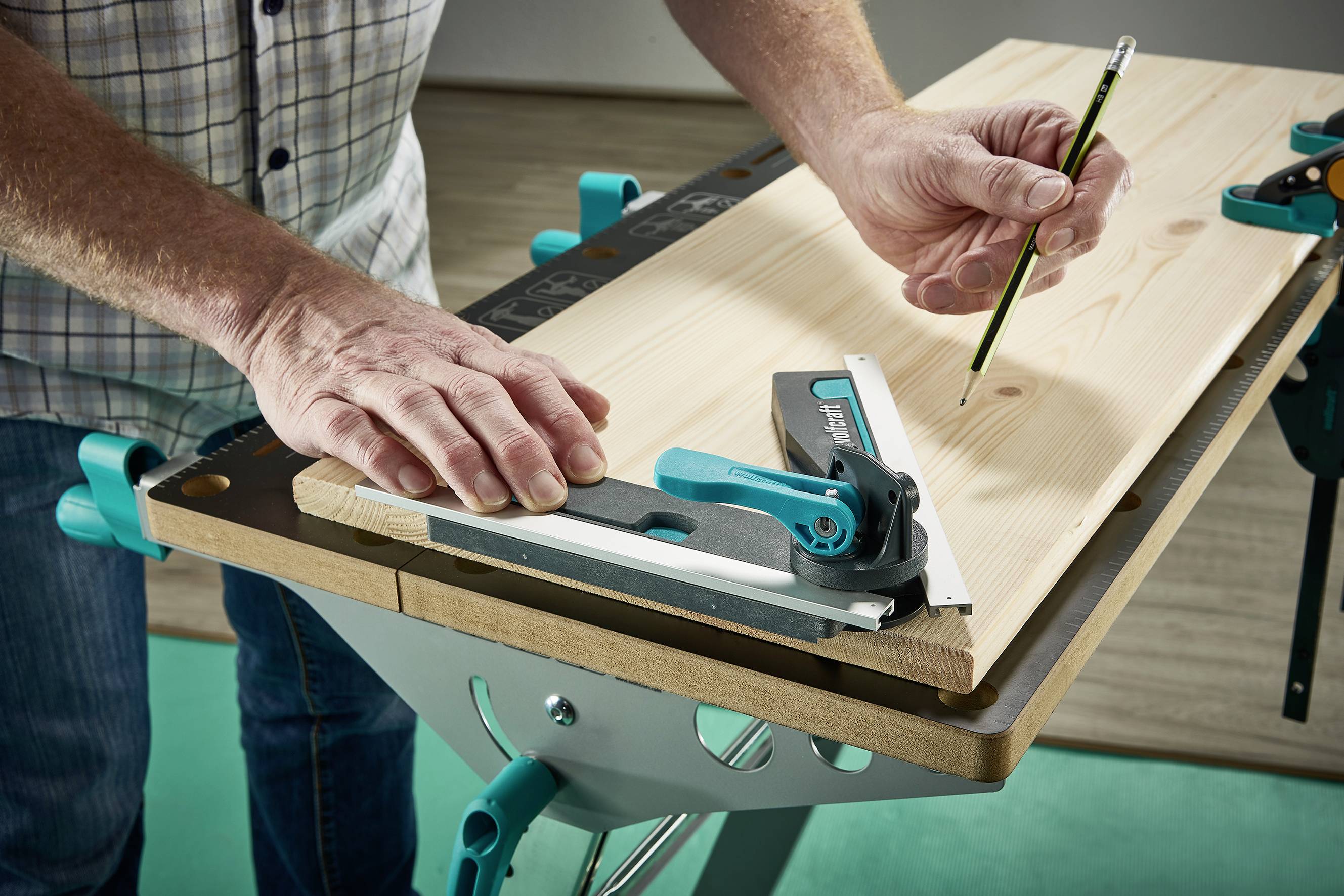 Osoba zaznacza ołówkiem deskę na stole warsztatowym. Do precyzyjnego ustawienia używany jest kątomierz.
