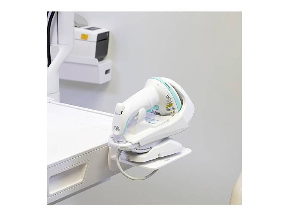 Skaner ręczny jest zamocowany na wózku medycznym. Na tylnym planie widoczne są kolejne urządzenia medyczne.