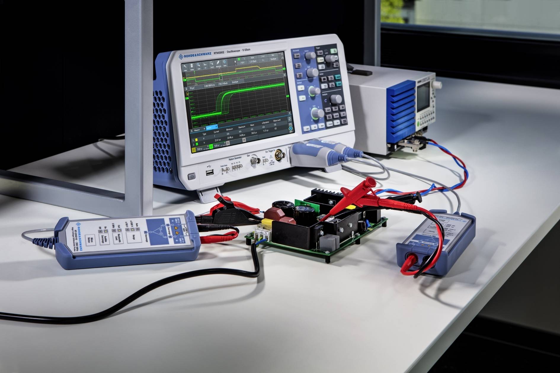 'Oscyloskop przedstawia graficzną reprezentację sygnałów napięciowych w połączeniu z elementami elektronicznymi na stole.'