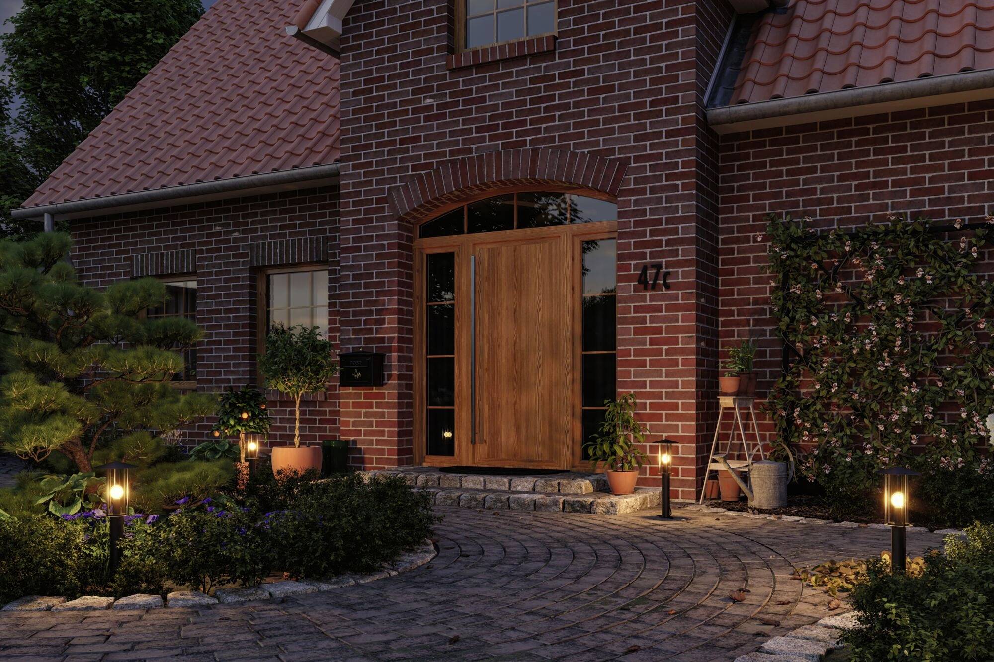 Ceglany dom w kolorze czerwonym z drewnianą furtką, otoczony roślinami i oświetlony latarniami ogrodowymi o zmierzchu.