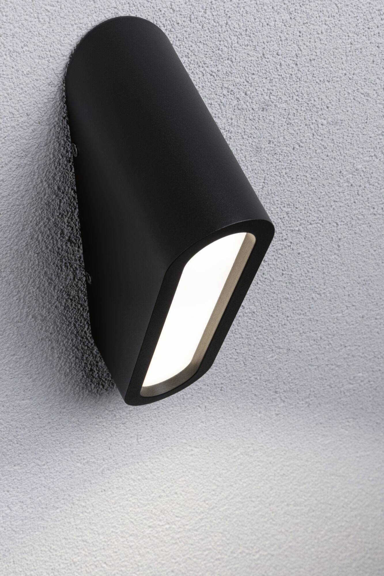Czarna kinkietowa lampa świeci na tle strukturalnej szarej ściany, tworząc miękką refleksję świetlną poniżej.