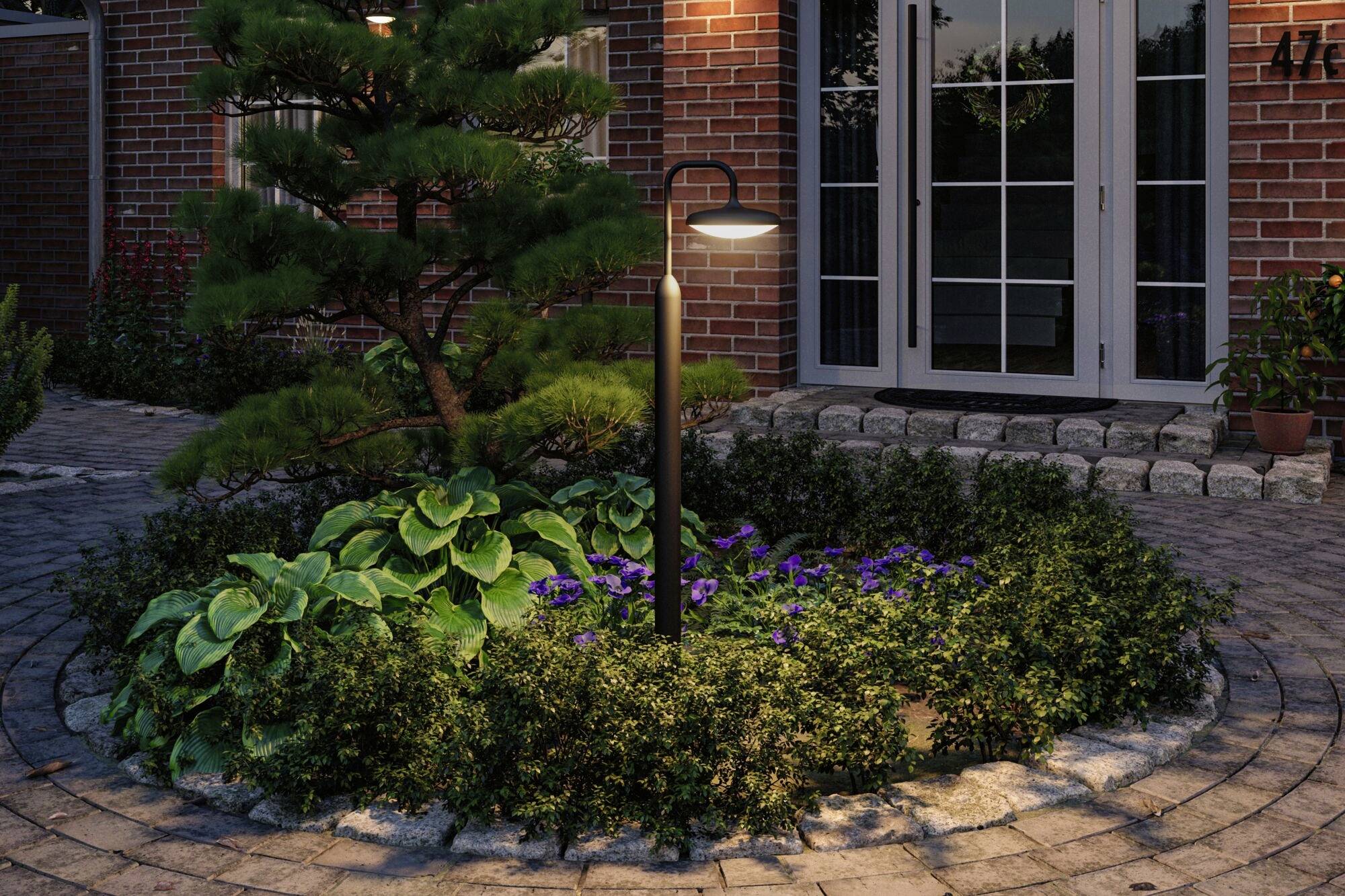 Oświetlony, okrągły teren ogrodowy z roślinami przed budynkiem z czerwonej cegły z podwójnymi drzwiami, wieczorem.