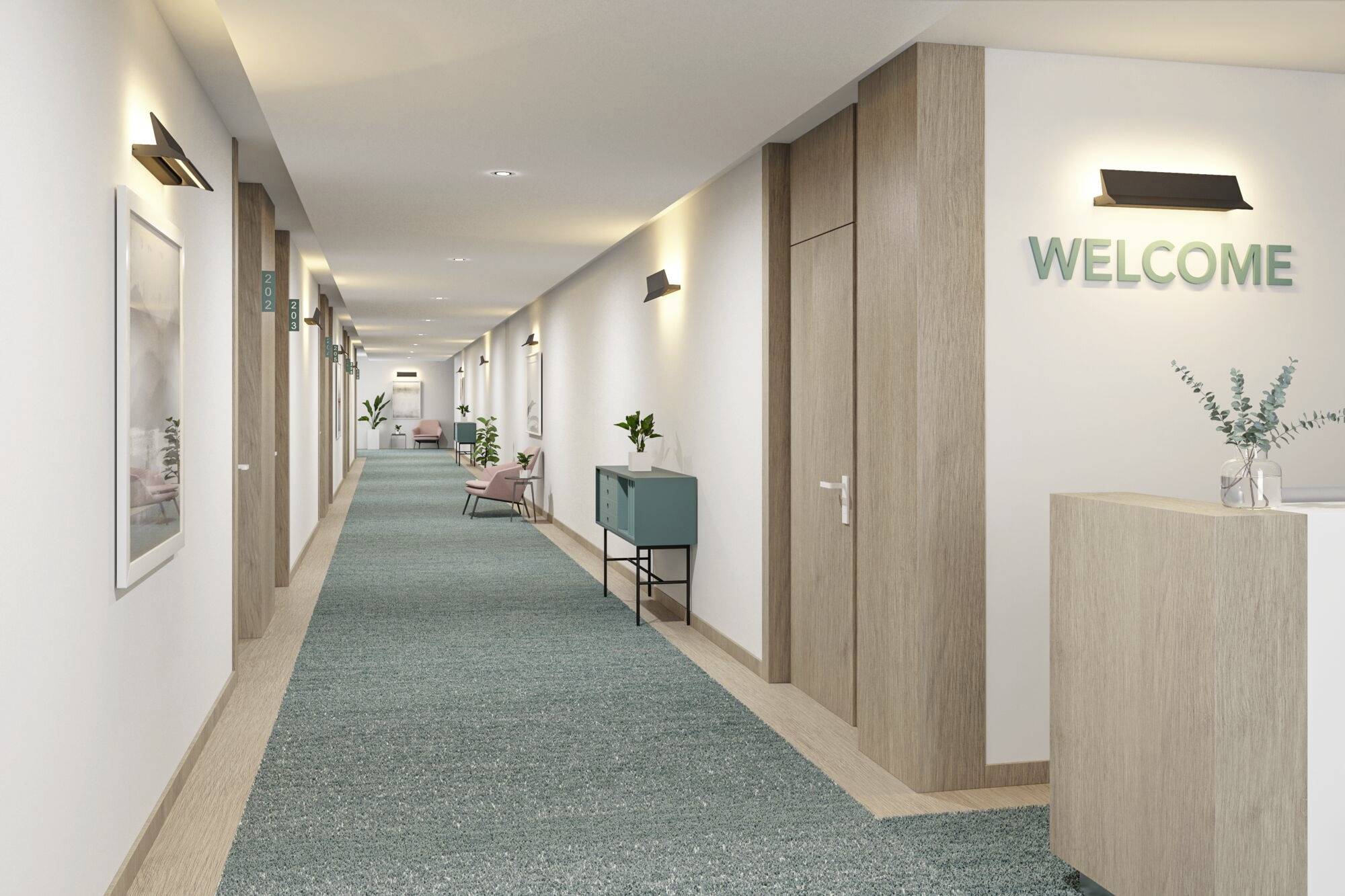 Długi korytarz hotelowy z zielonym dywanem, w nowoczesnym stylu. Na ścianie napis 'WELCOME'. Po lewej stronie wiszą oprawione obrazy i stoją rośliny.