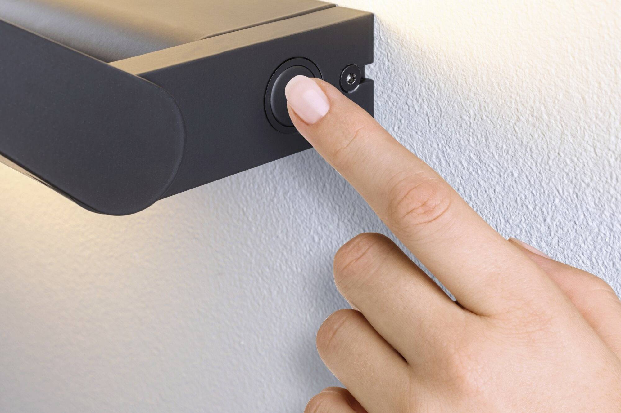 Palec naciska czarny przycisk z boku elektrycznego urządzenia zamontowanego na ścianie.