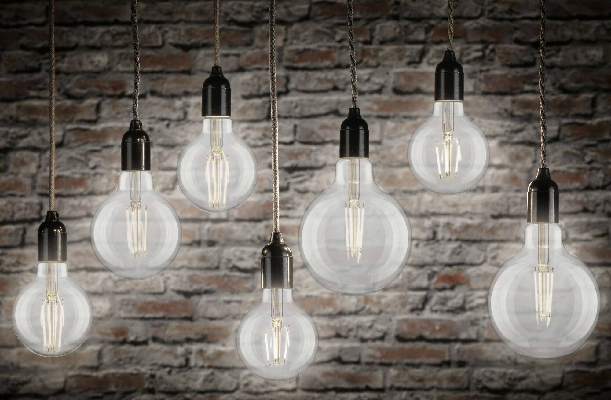 Osiem wiszących żarówek przed murem z cegły, niektóre z nich świecą. Ciepłe światło tworzy przytulną atmosferę.