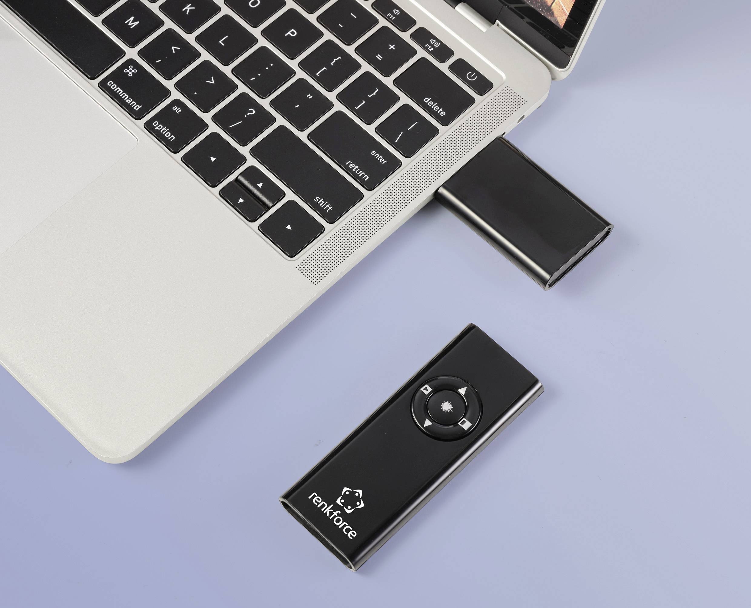 Laptop z podłączonym czarnym pilotem; obok leży pendrive. Pilot posiada przyciski kierunkowe.