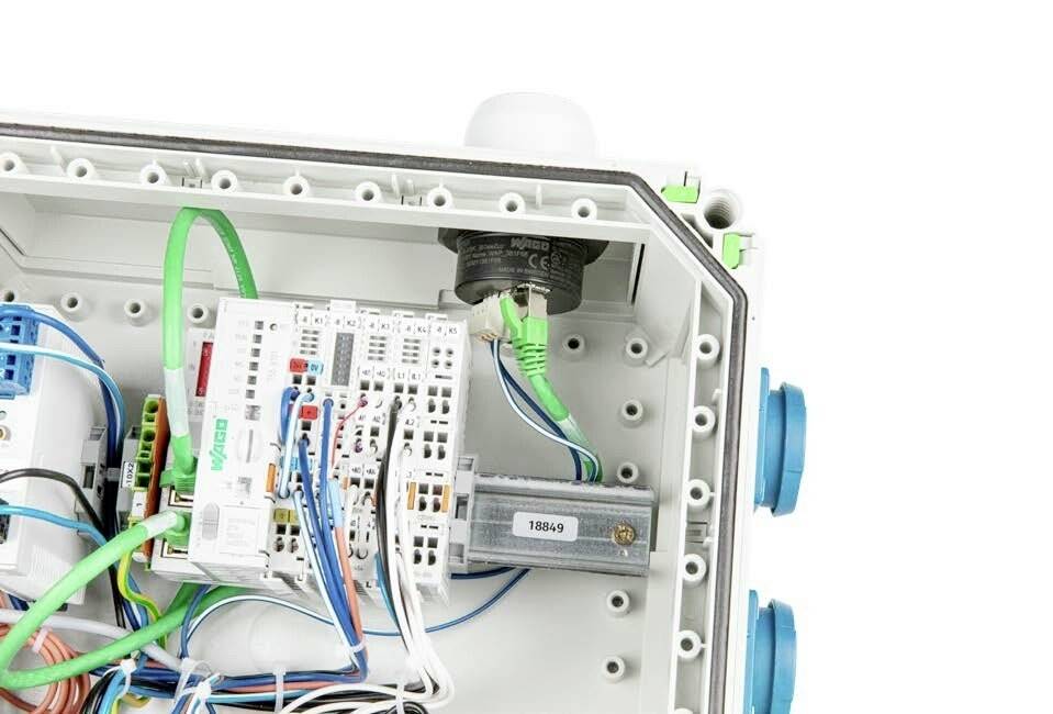 Widok wewnętrzny otwartej skrzynki rozdzielczej z przewodami, routerem i różnymi elementami elektrycznymi.