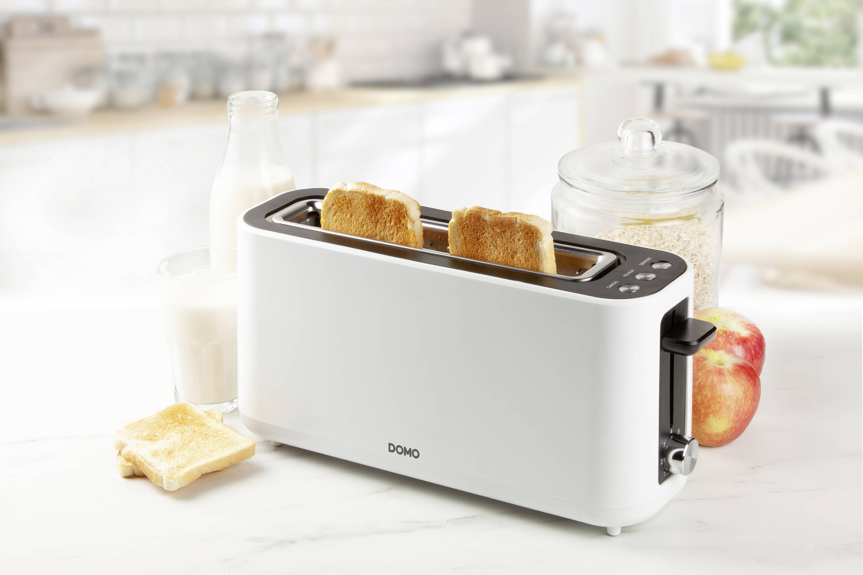 Biały toster stoi w kuchni i opiekа dwie kromki chleba. Obok niego szklanka mleka, szklanka owsa oraz dwa jabłka.