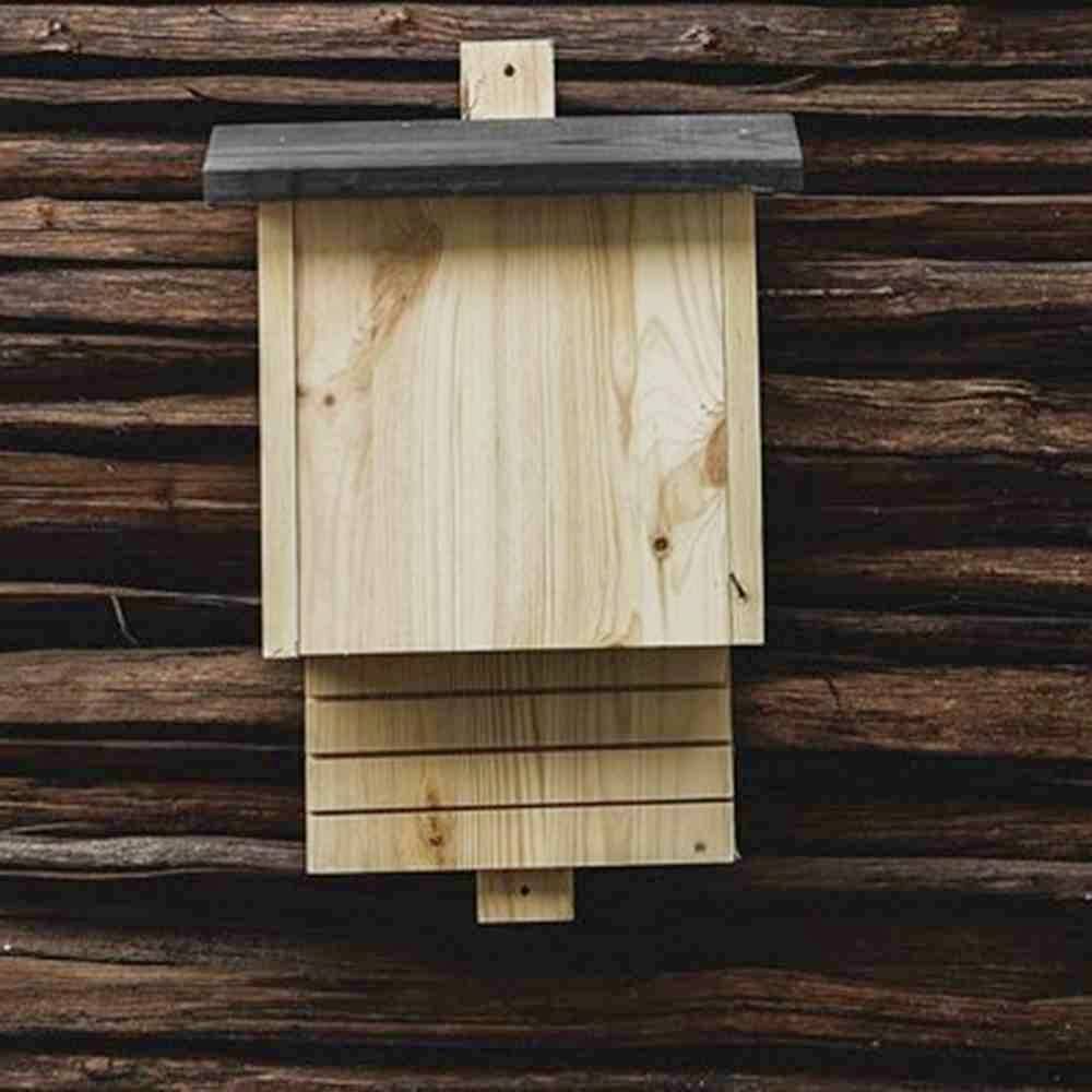 Drewniany domek lęgowy dla nietoperzy zamontowany na brązowej ścianie drewnianej.