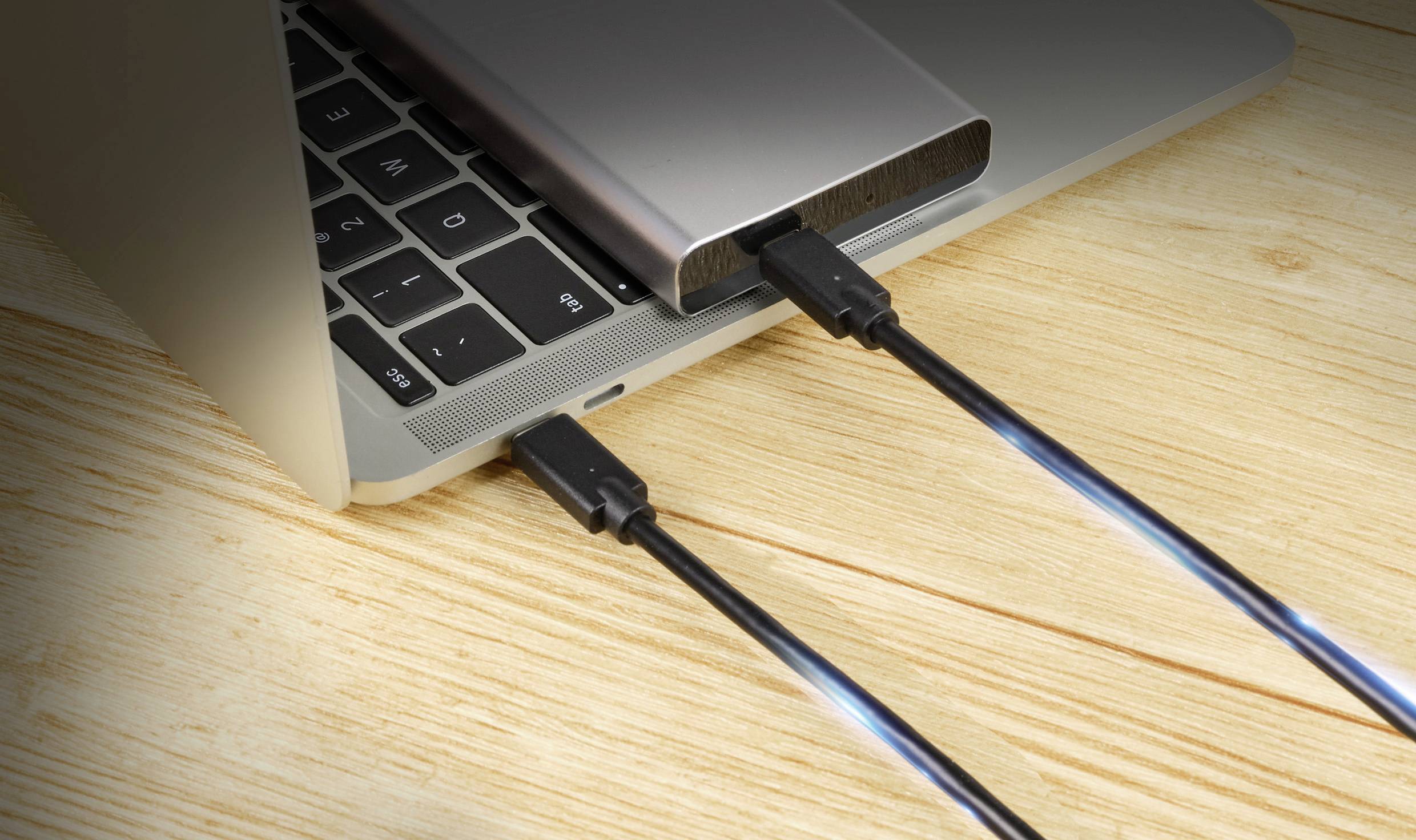 Laptop jest podłączony do zewnętrznej obudowy dysku twardego, która leży na drewnianym stole. Dwa kable USB są podłączone.