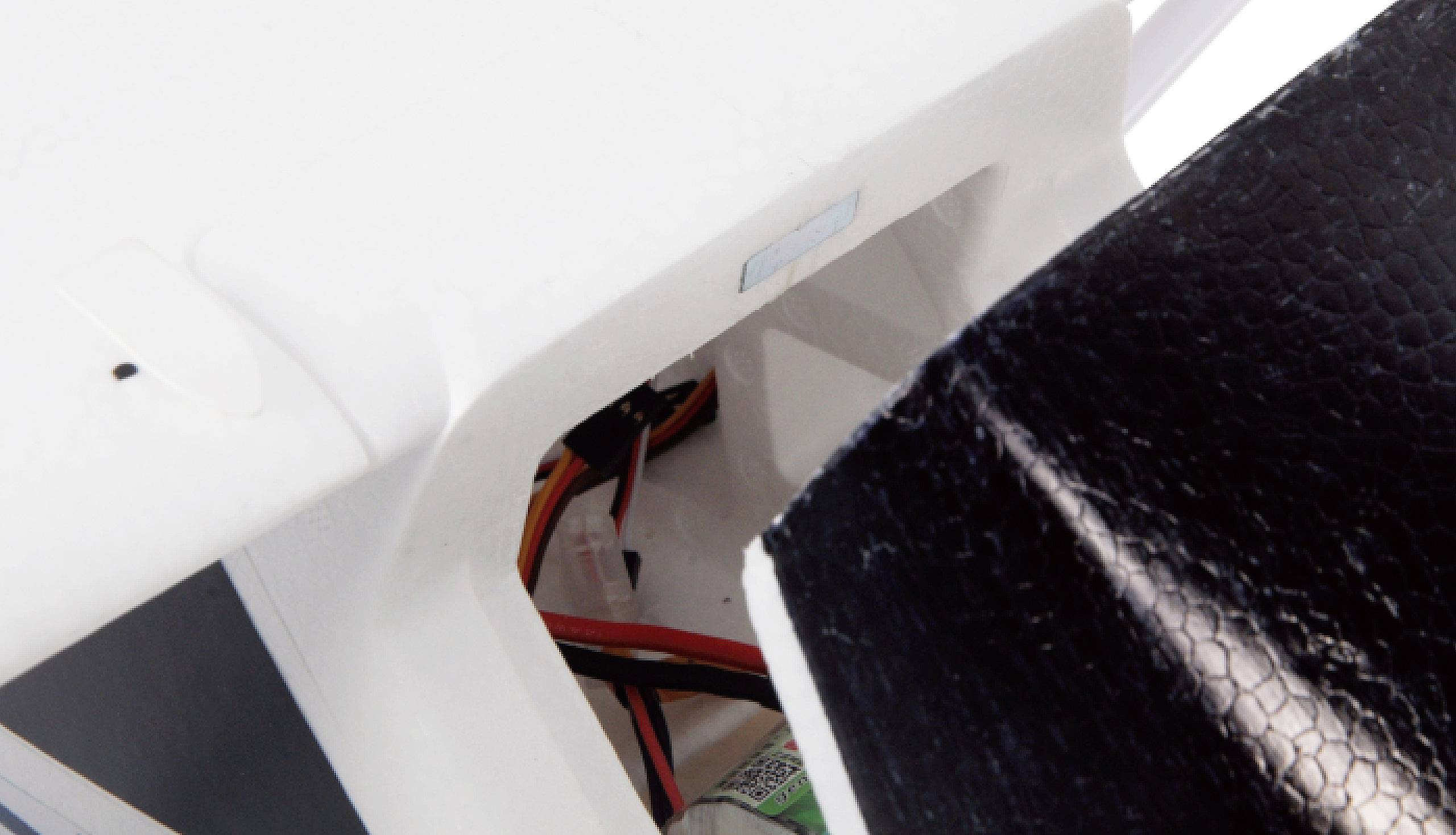 Biała struktura plastikowa modelu samolotu z widocznymi przewodami wewnątrz oraz częściowo czarną powierzchnią po prawej stronie.