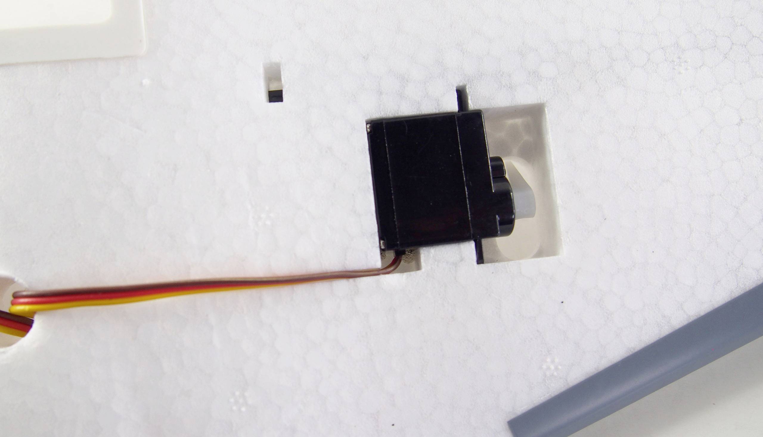 Czarne urządzenie z przewodami na białym tle, prawdopodobnie element elektryczny lub silnik, podłączony kolorowymi przewodami.