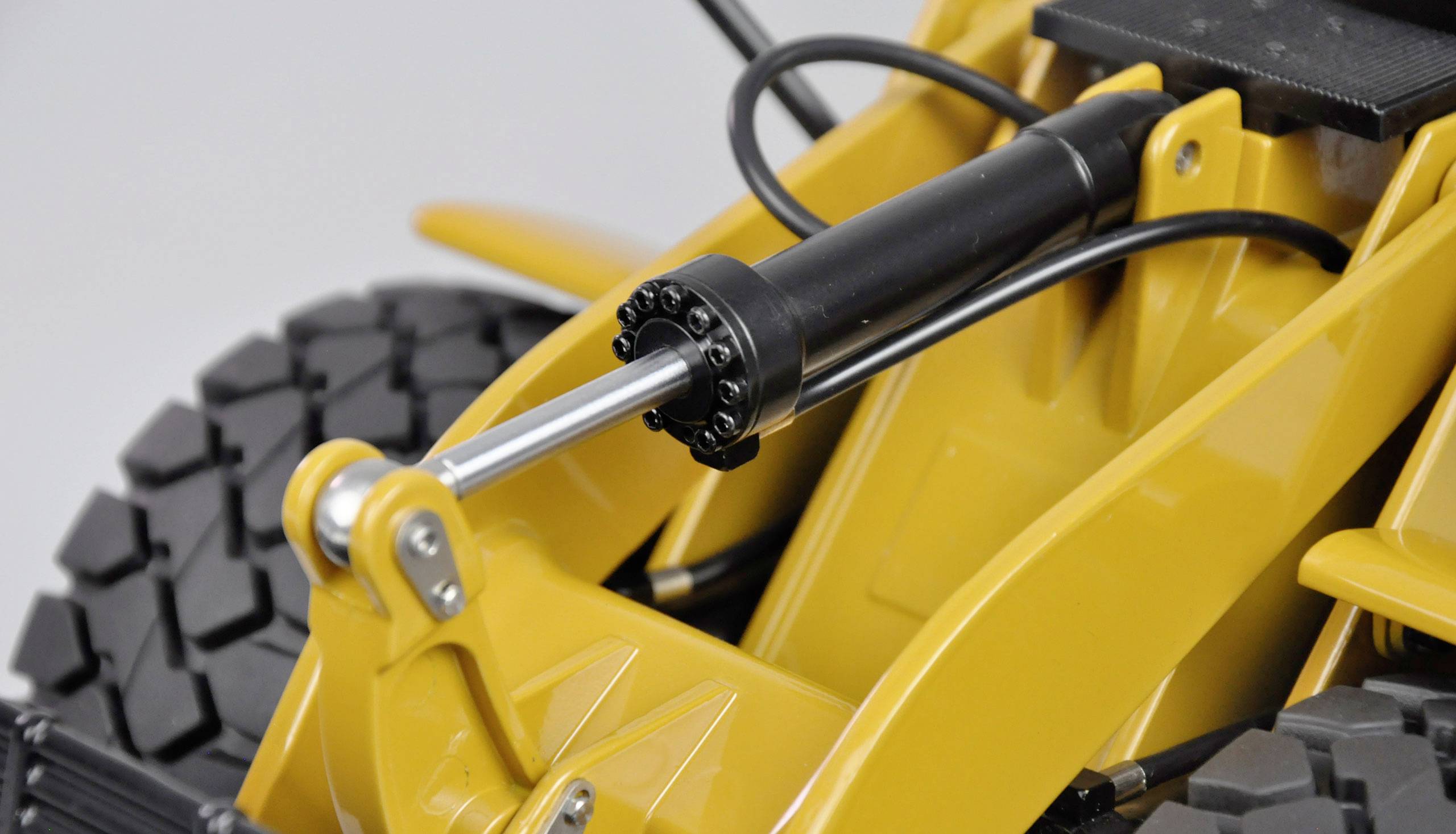 Żółty koparka z naciskiem na cylinder hydrauliczny i duże koła.