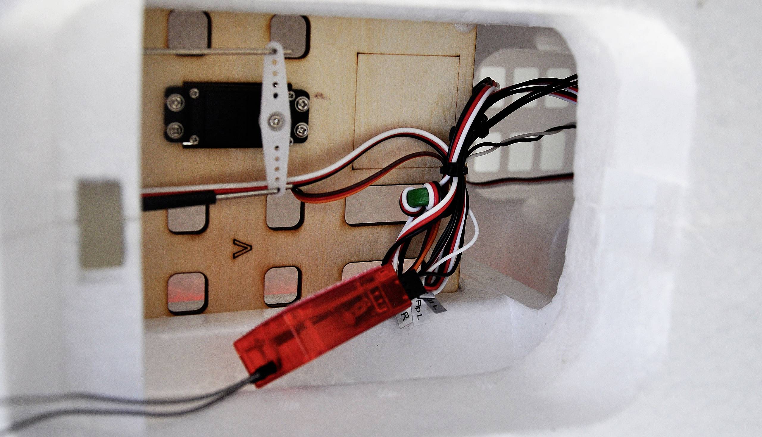 Widok wewnętrzny białego modelu samolotu. Pokazuje komponenty elektroniczne: serwomechanizm, przewody i czerwone pudełko odbiornika.