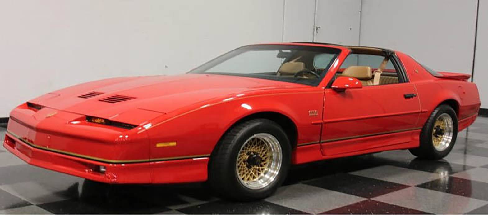 Czerwone sportowe coupé w stylu retro, prezentujące wyrazistą sylwetkę nadwozia i złote felgi, zaparkowane w przestrzeni wystawowej.