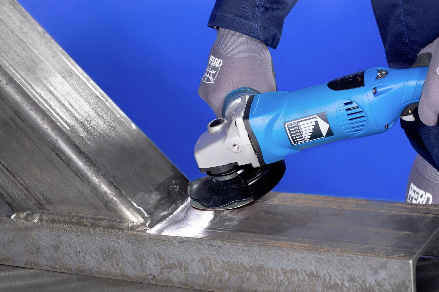 Osoba szlifuje spawaną spoinę metalową na konstrukcji stalowej za pomocą niebieskiej szlifierki kątowej.