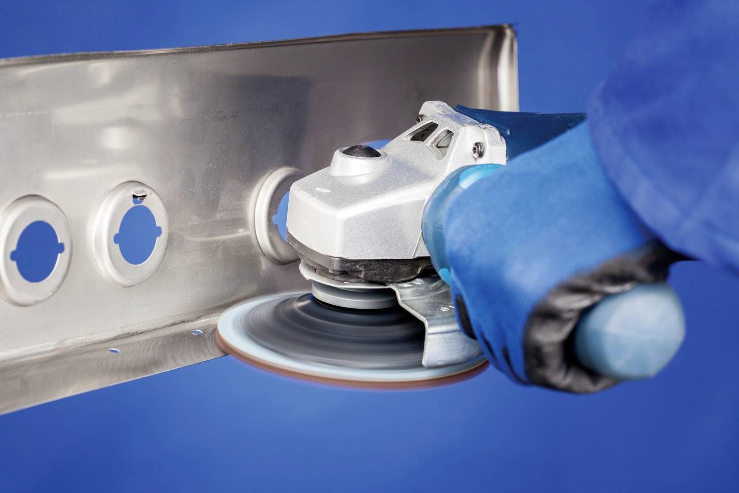 Osoba w niebieskich rękawiczkach szlifuje płytę metalową szlifierką kątową.