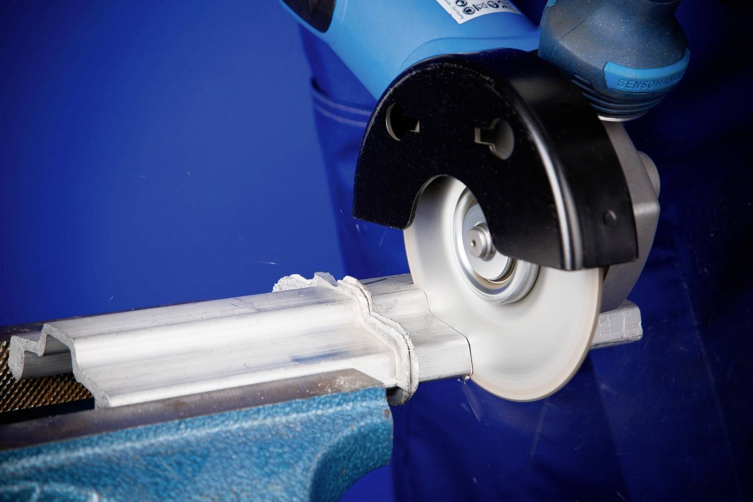 Szlifierka kątowa tnie rurę metalową zaciśniętą w imadle. Podczas cięcia pojawiają się iskry.