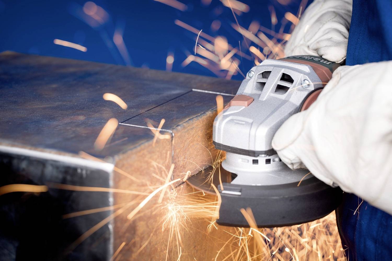 Robotnik szlifuje metal kątnówką, podczas gdy iskry lecą. Zbliżenie sceny pracy w warsztacie.