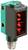 Prostokątny czujnik z czerwoną soczewką czołową, zielona obudowa i metalowe złącze. Służy do rozpoznawania obiektów w zastosowaniach przemysłowych.