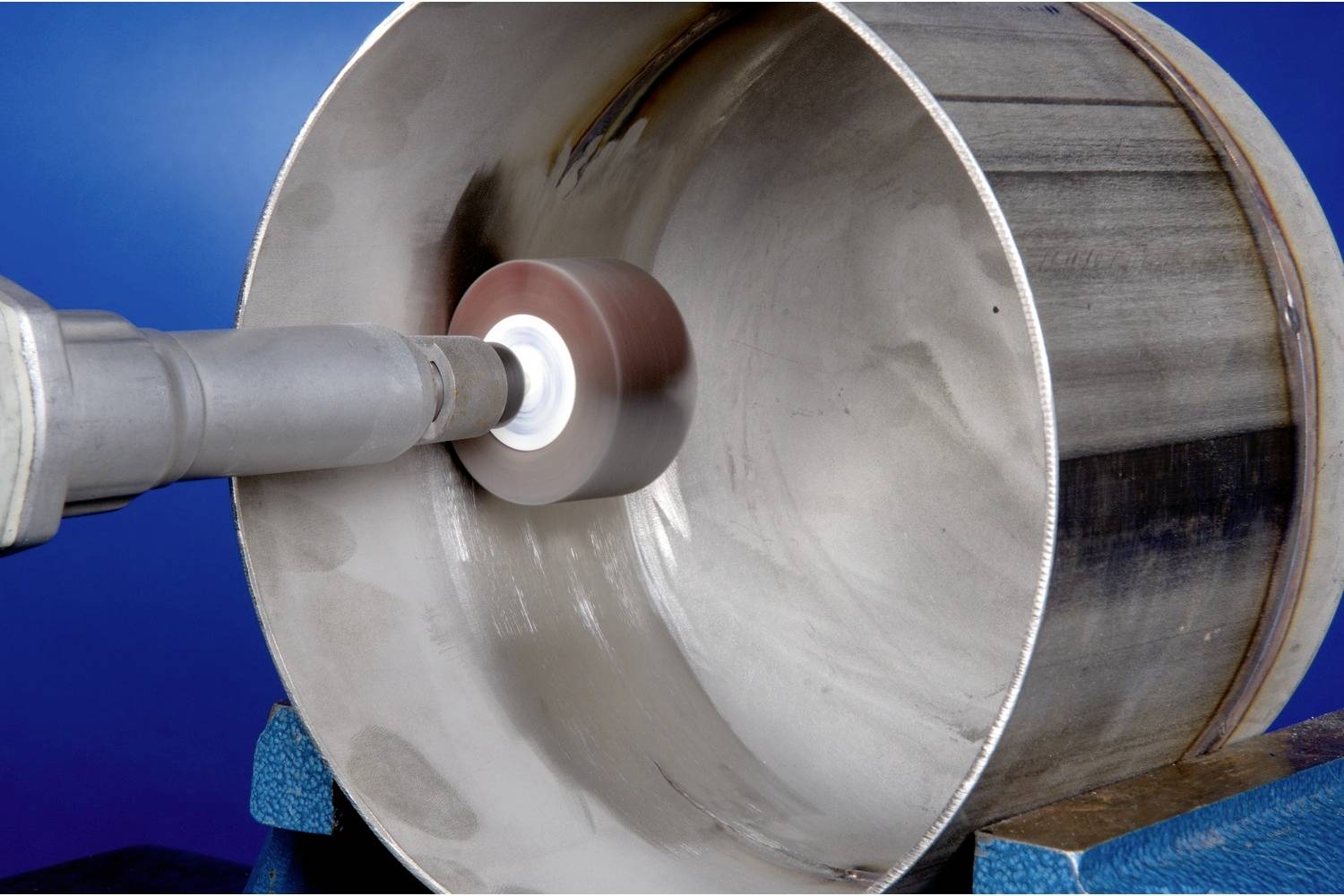 Metalowa maszyna poleruje wnętrze dużej cylindrycznej rury. Tło jest niebieskie.