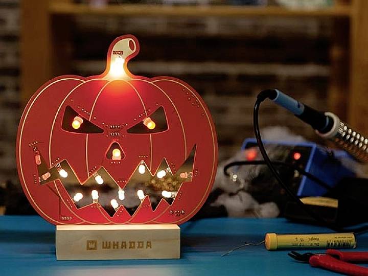 Element dekoracyjny na Halloween w postaci podświetlonej dyni z twarzą, wyposażony w elektroniczne komponenty, leżący na stole z narzędziami.