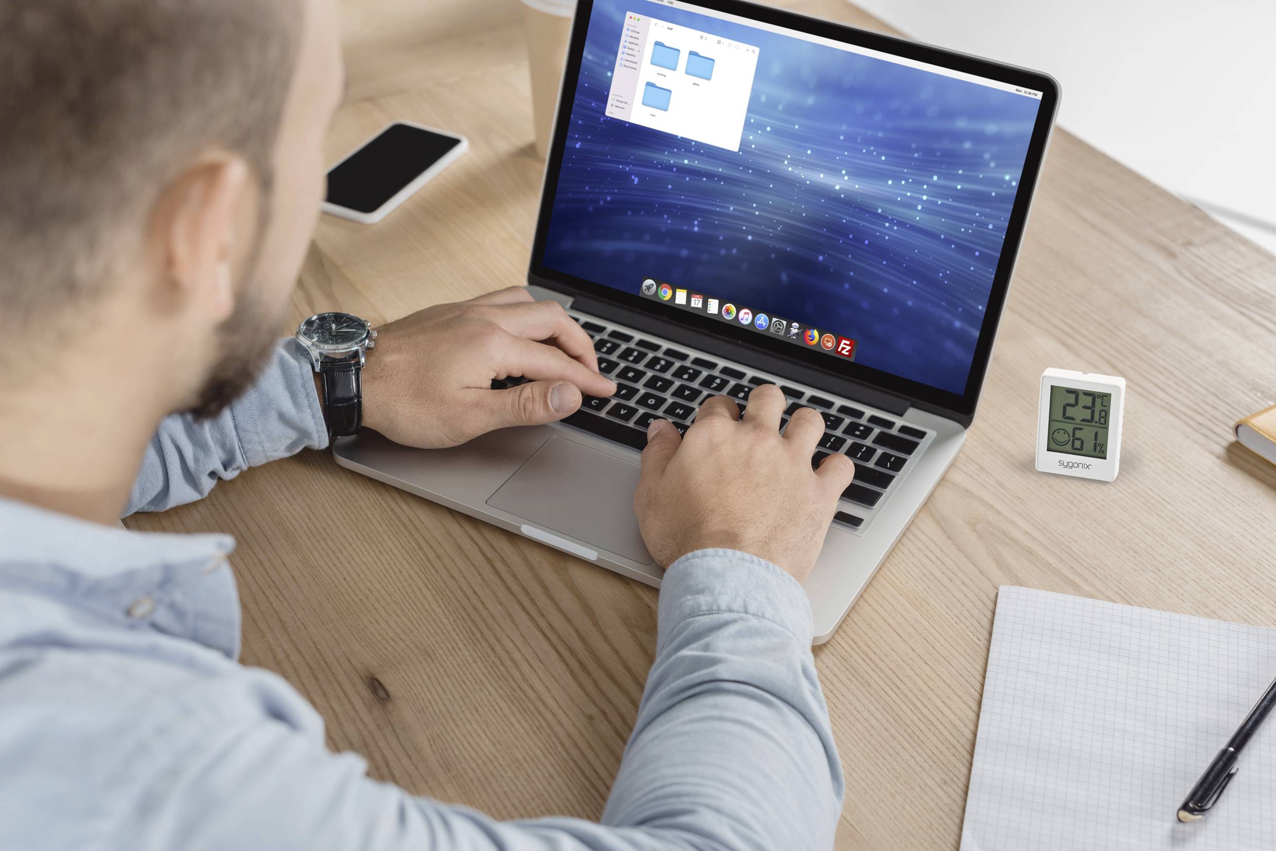 Mężczyzna pracuje na laptopie przy biurku, otoczony smartfonem, kubkiem i notatnikiem.