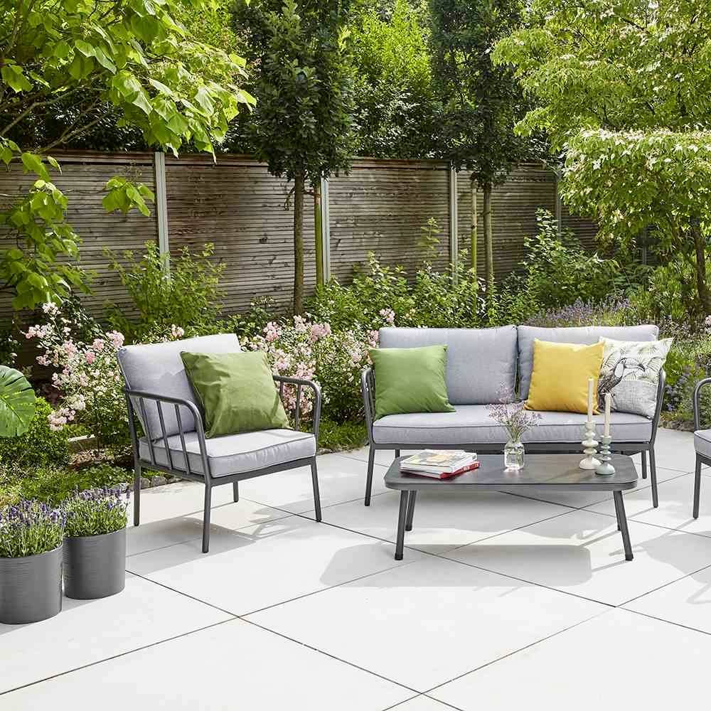 Zestaw mebli ogrodowych na tarasie, składający się z dwóch foteli, sofy i stolika. Otoczony roślinami i drewnianym płotem w tle.