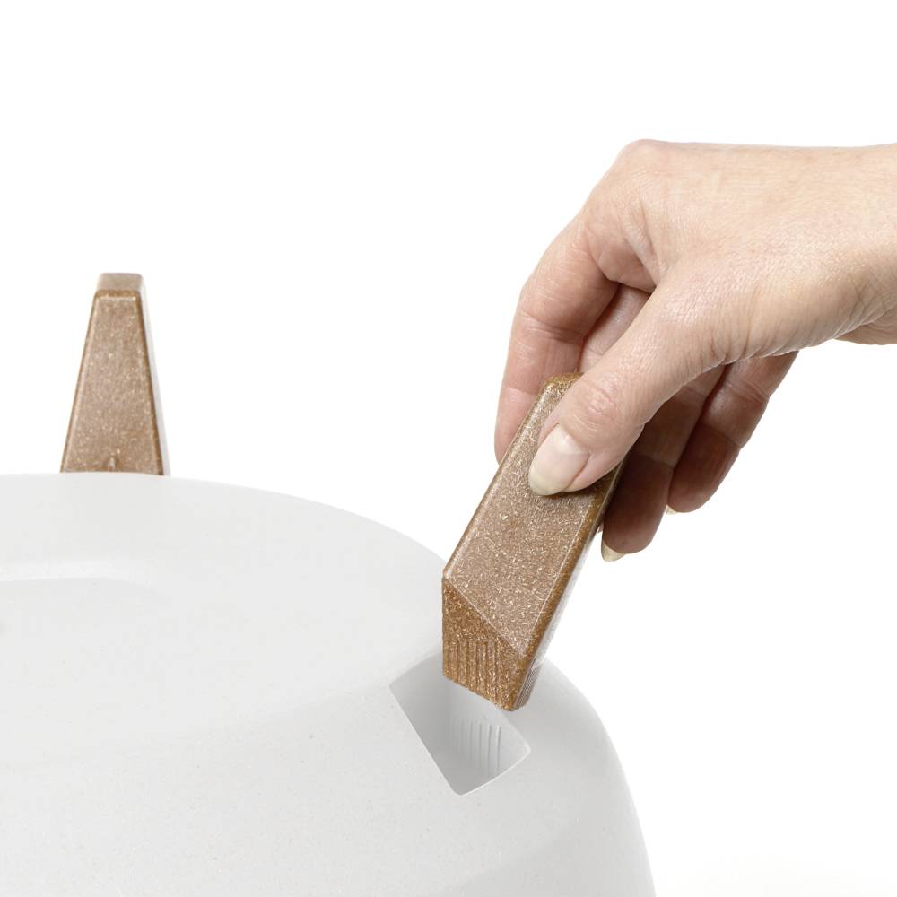 Dłoń sięga po prostokątny, brązowy przedmiot, który kładzie się na białej, gładkiej powierzchni.