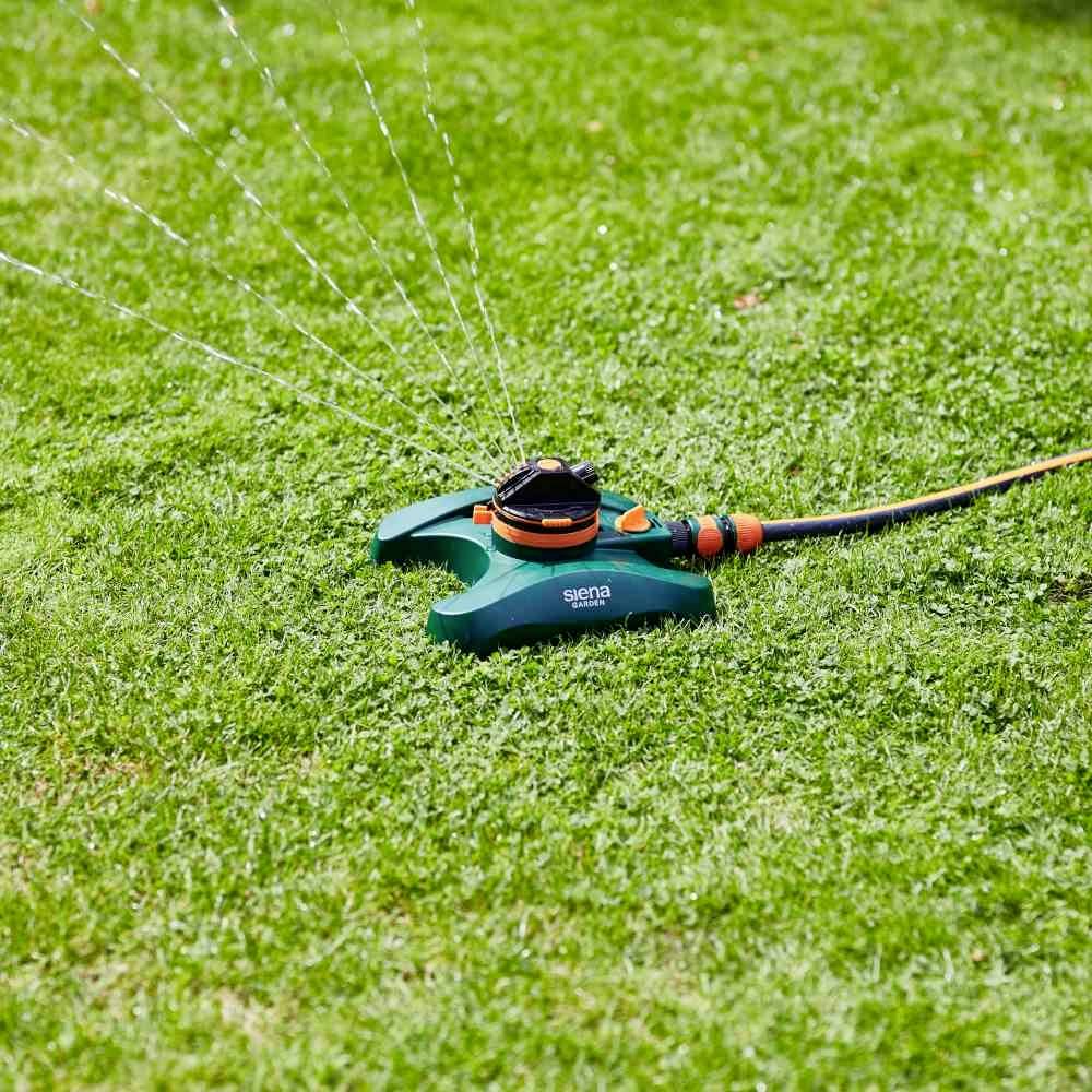 Automatyczny zraszacz na zielonej trawie rozpyla wodę w kilku kierunkach.