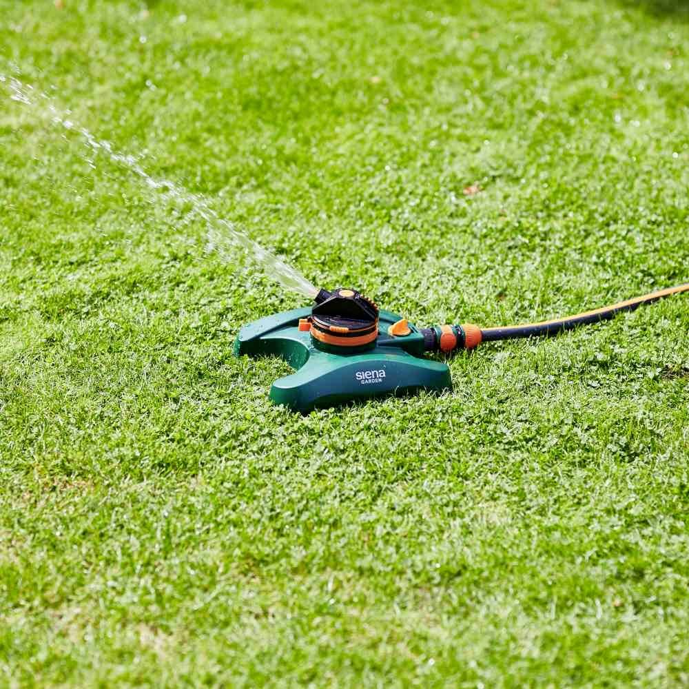 Zielony zraszacz równomiernie nawadnia trawnik w słoneczny dzień.