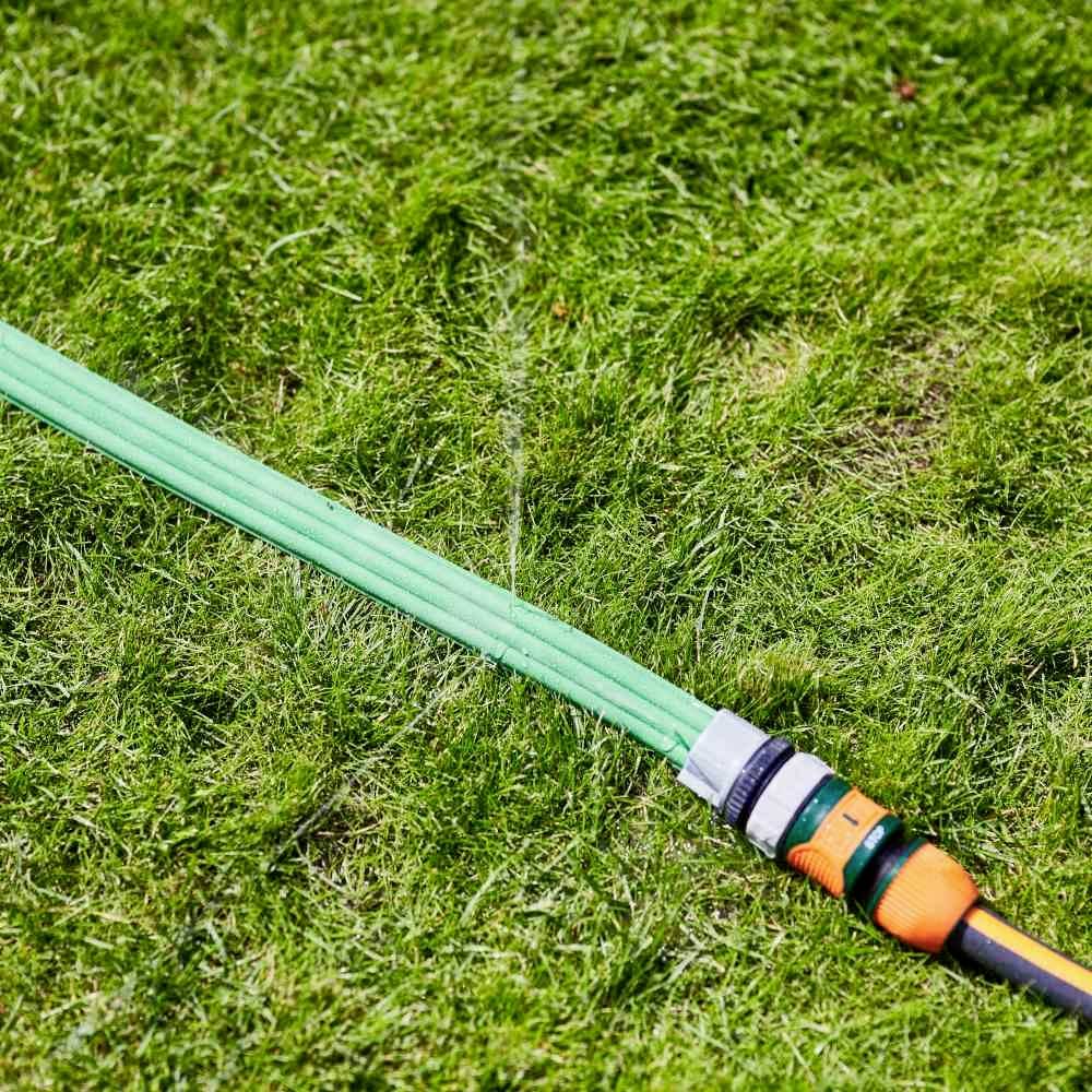 Zielony wąż ogrodowy leży na trawniku i jest podłączony do kranu. Woda delikatnie kapie z końca węża.