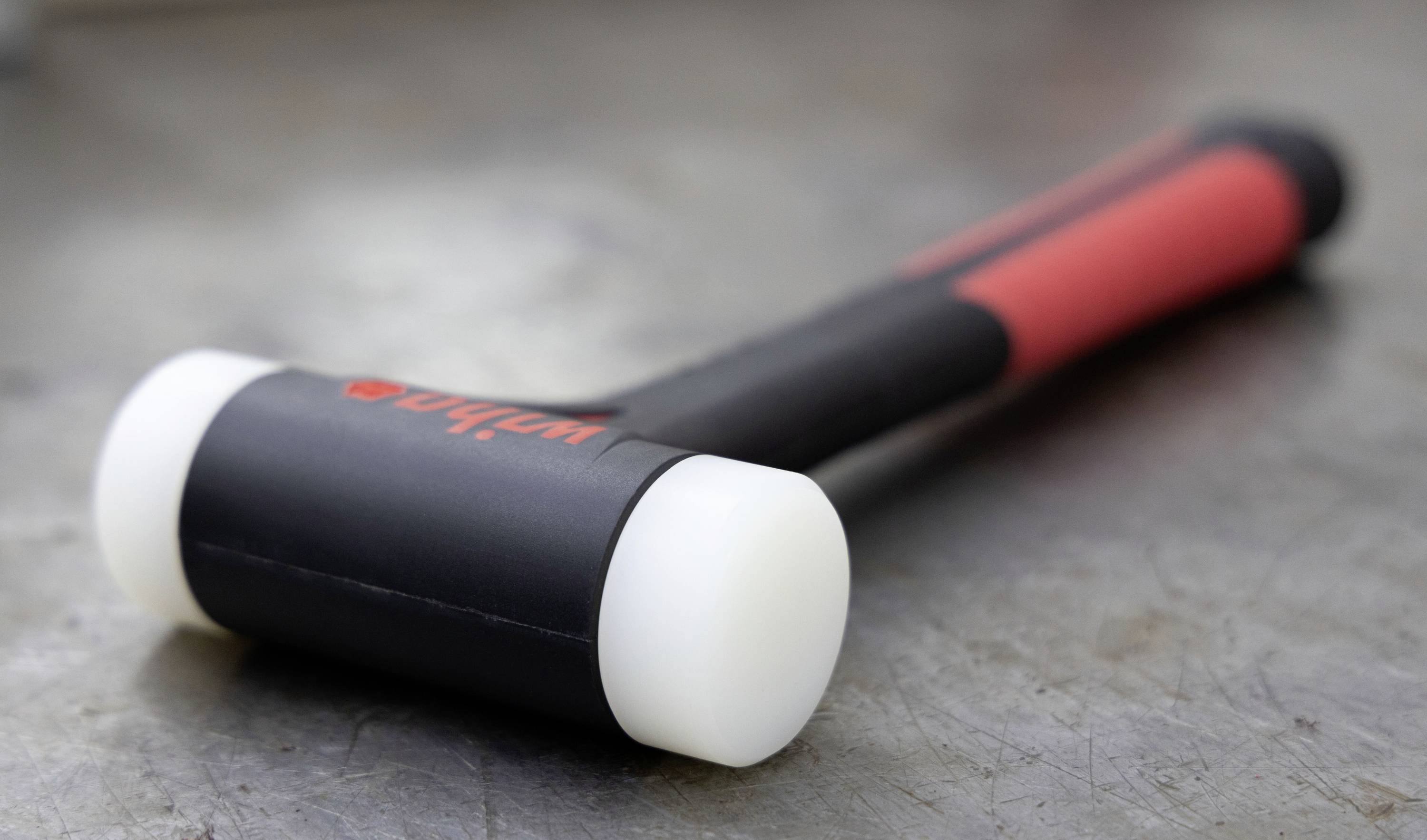 Czarny młotek z czerwonymi akcentami i białymi plastikowymi głowicami na metalowej powierzchni.