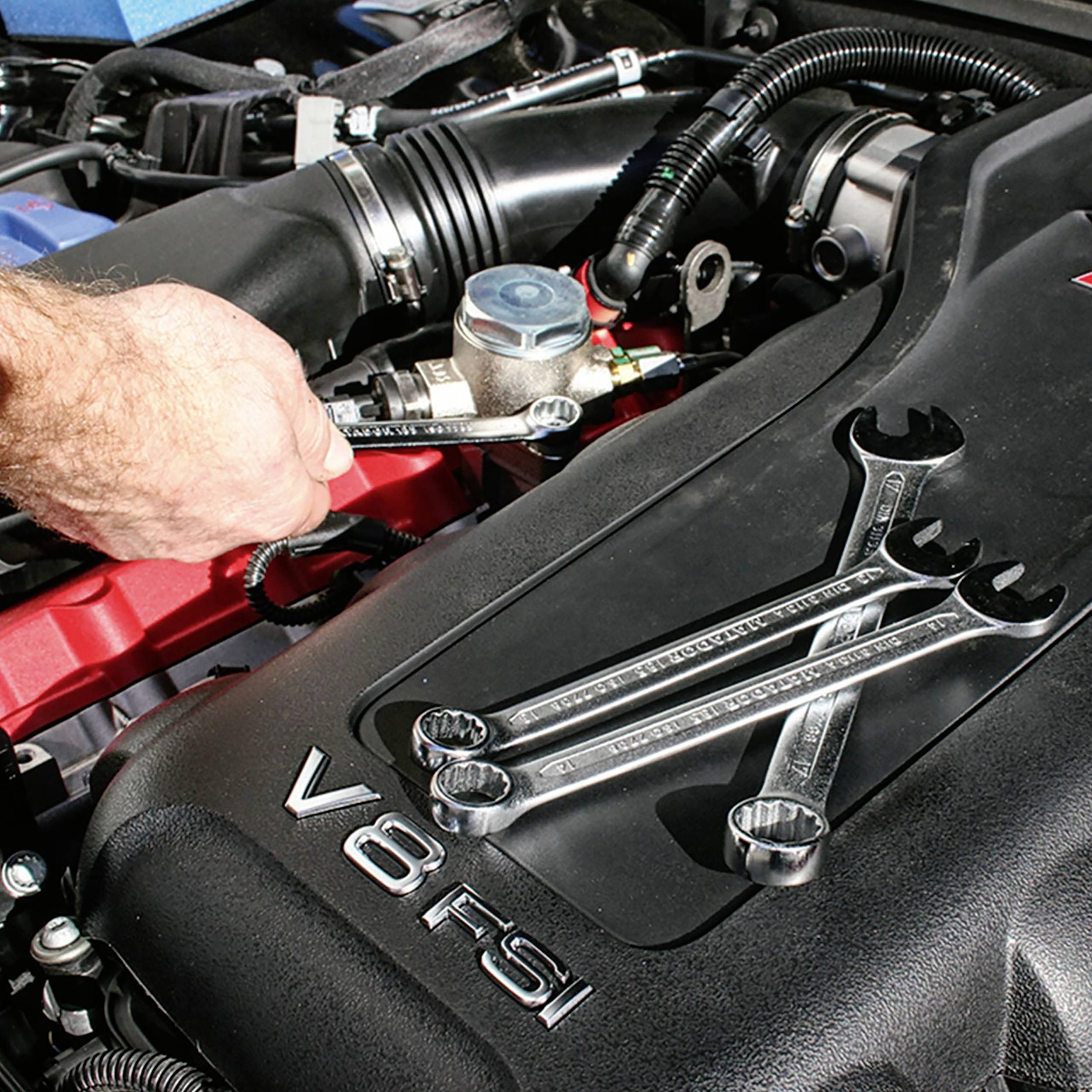 Jedna osoba pracuje kluczem mechanicznym przy silniku samochodu. Dwa klucze leżą na bloku silnika V8 FSI.