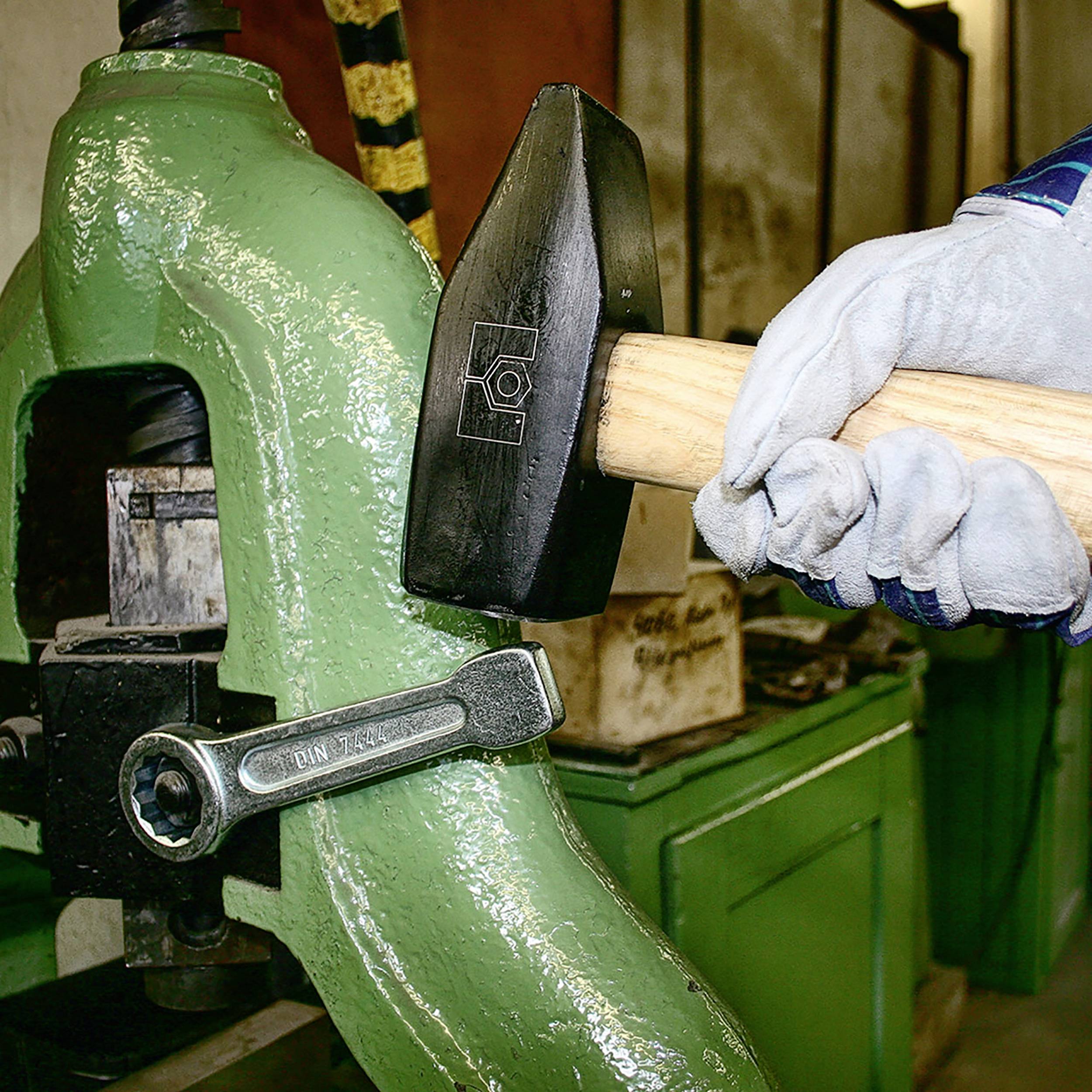 Robotnik przemysłowy obsługuje prasę mechaniczną za pomocą młotka i w rękawicach w warsztacie.