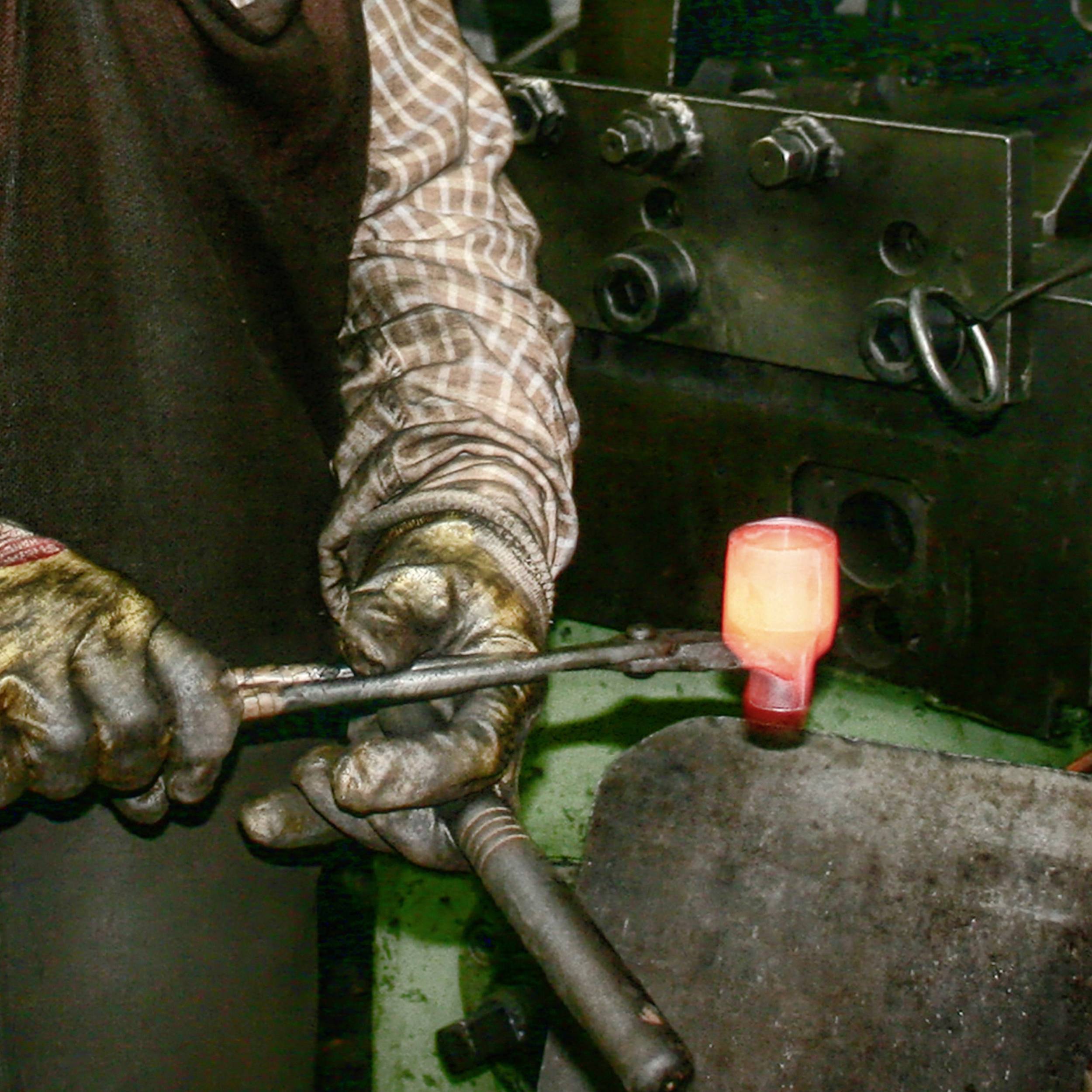 Kowal obrabia rozżarzone kawałek metalu na kowadle w warsztacie. Nosi odzież ochronną, zbliżenie na wykonywaną pracę.