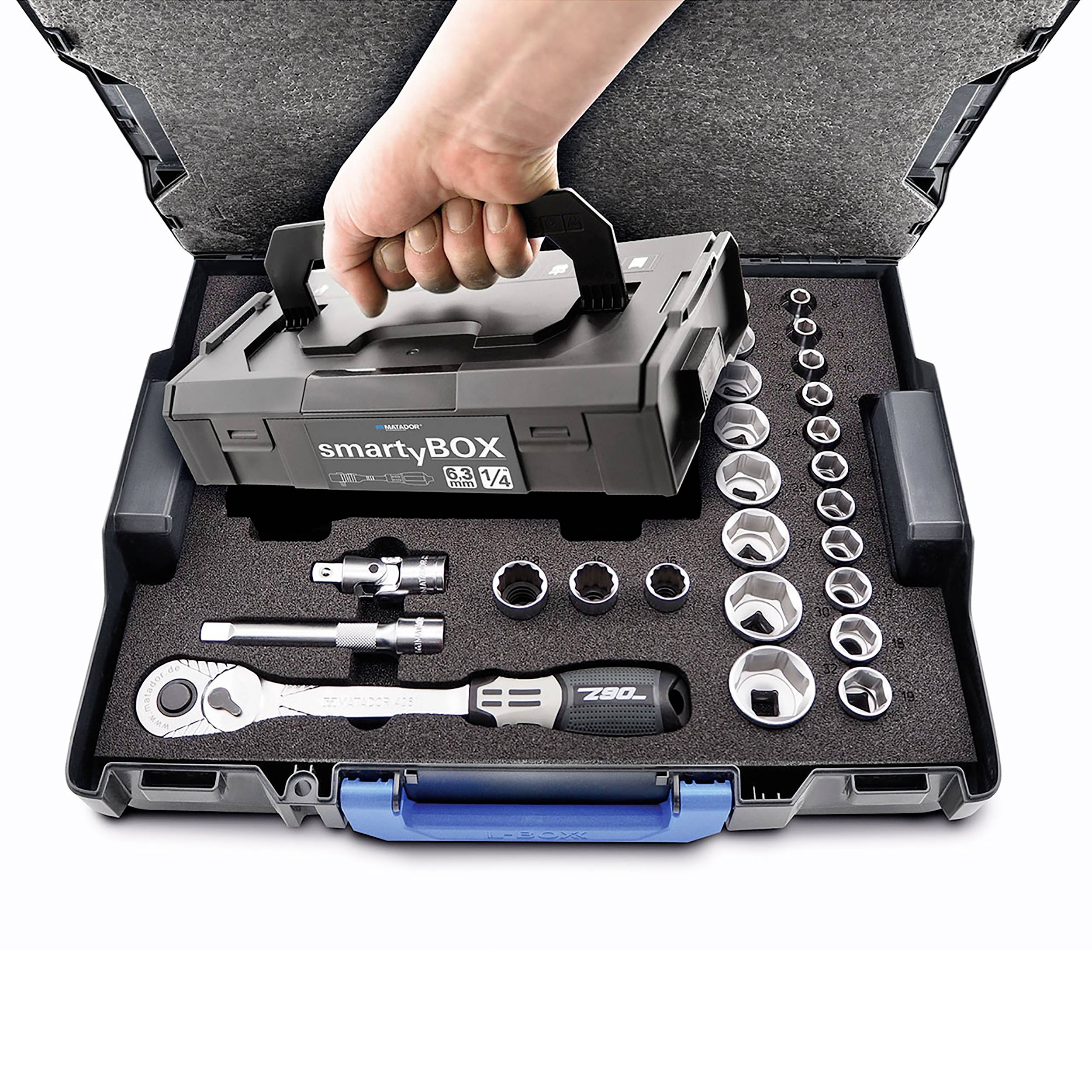 Ręka trzyma szary skrzynkę narzędziową (smartyBOX) z otwartą pokrywą, w której widoczne są różne klucze nasadowe i narzędzia.