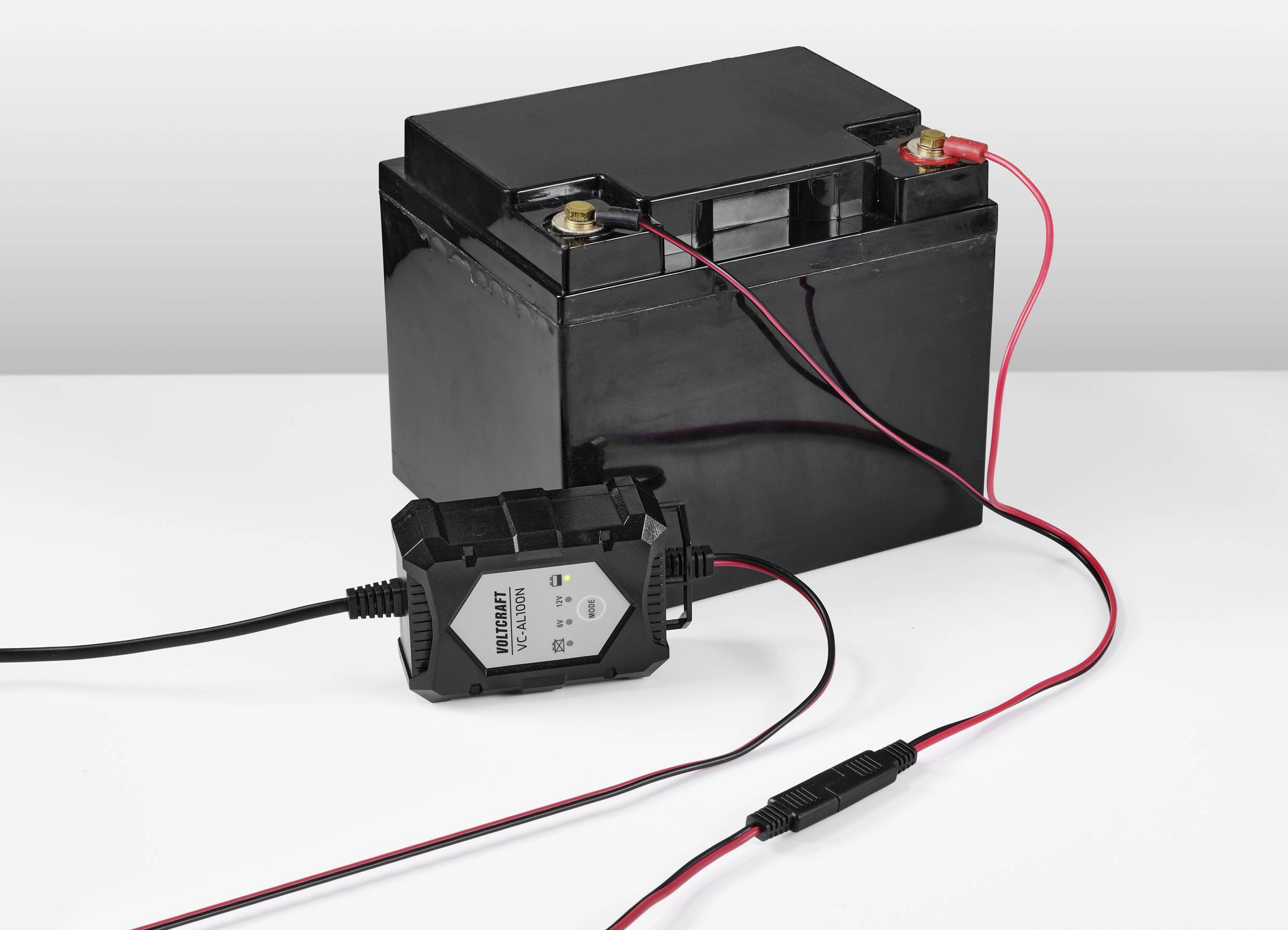 Czarna bateria samochodowa jest podłączona do ładowarki. Czerwone i czarne kable łączą bieguny baterii z urządzeniem.