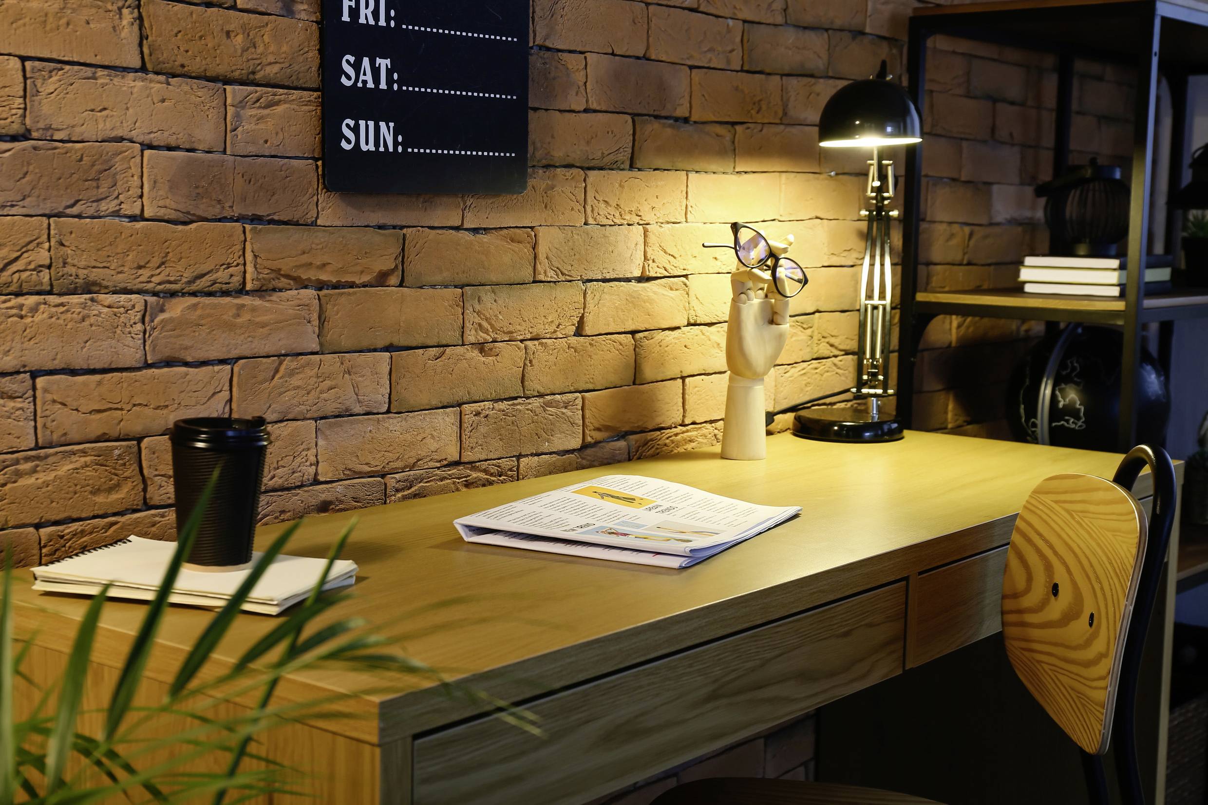 Przytulne biurko z lampką, stojakiem na okulary i otwartym magazynem. Plakat przedstawia dni tygodnia.