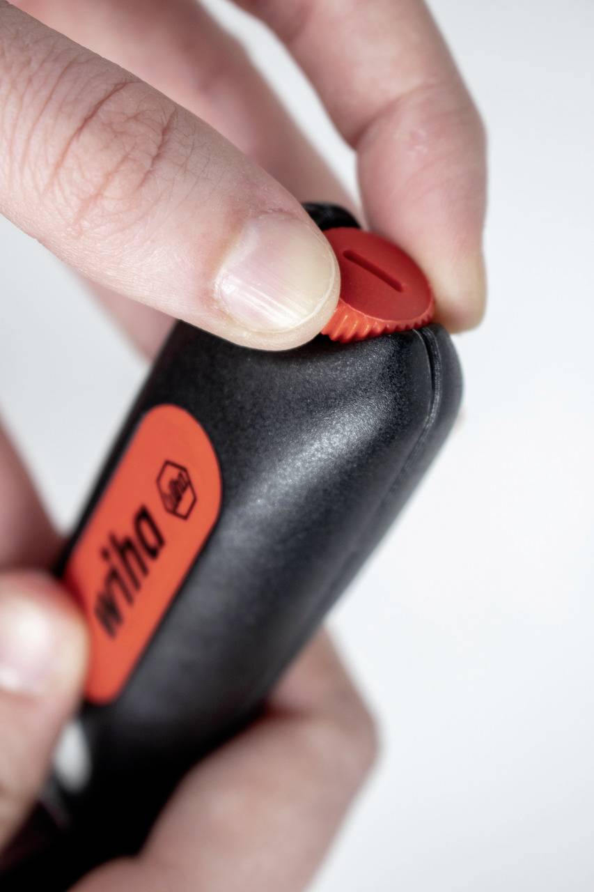 Jedna ręka reguluje czerwony pokrętło czarnego narzędzia. Na boku narzędzia widnieje logo.