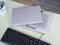Zamknięty laptop na podkładce chłodzącej na biurku obok klawiatury. W tle stoi pojemnik na długopisy.