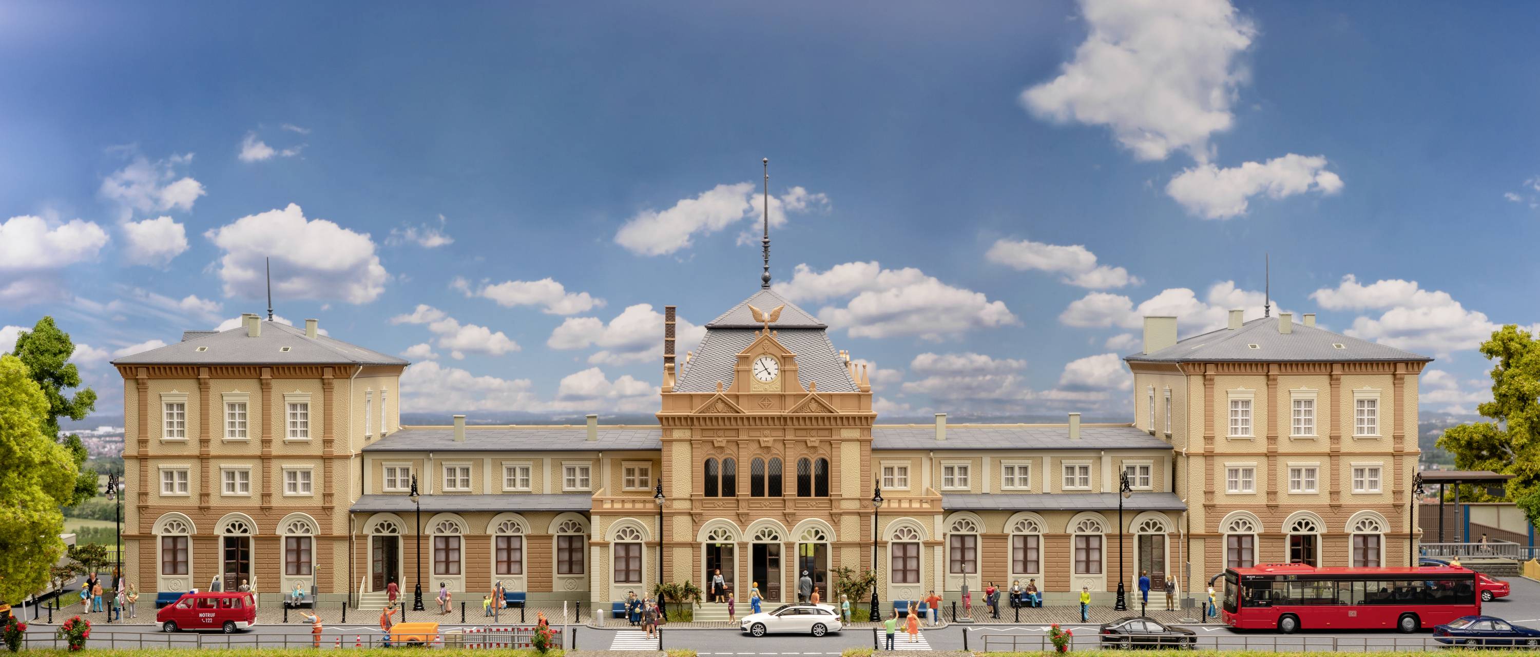 Model historycznego dworca kolejowego z dokładnie odwzorowanymi strukturami budynków, ludźmi i pojazdami na pierwszym planie.