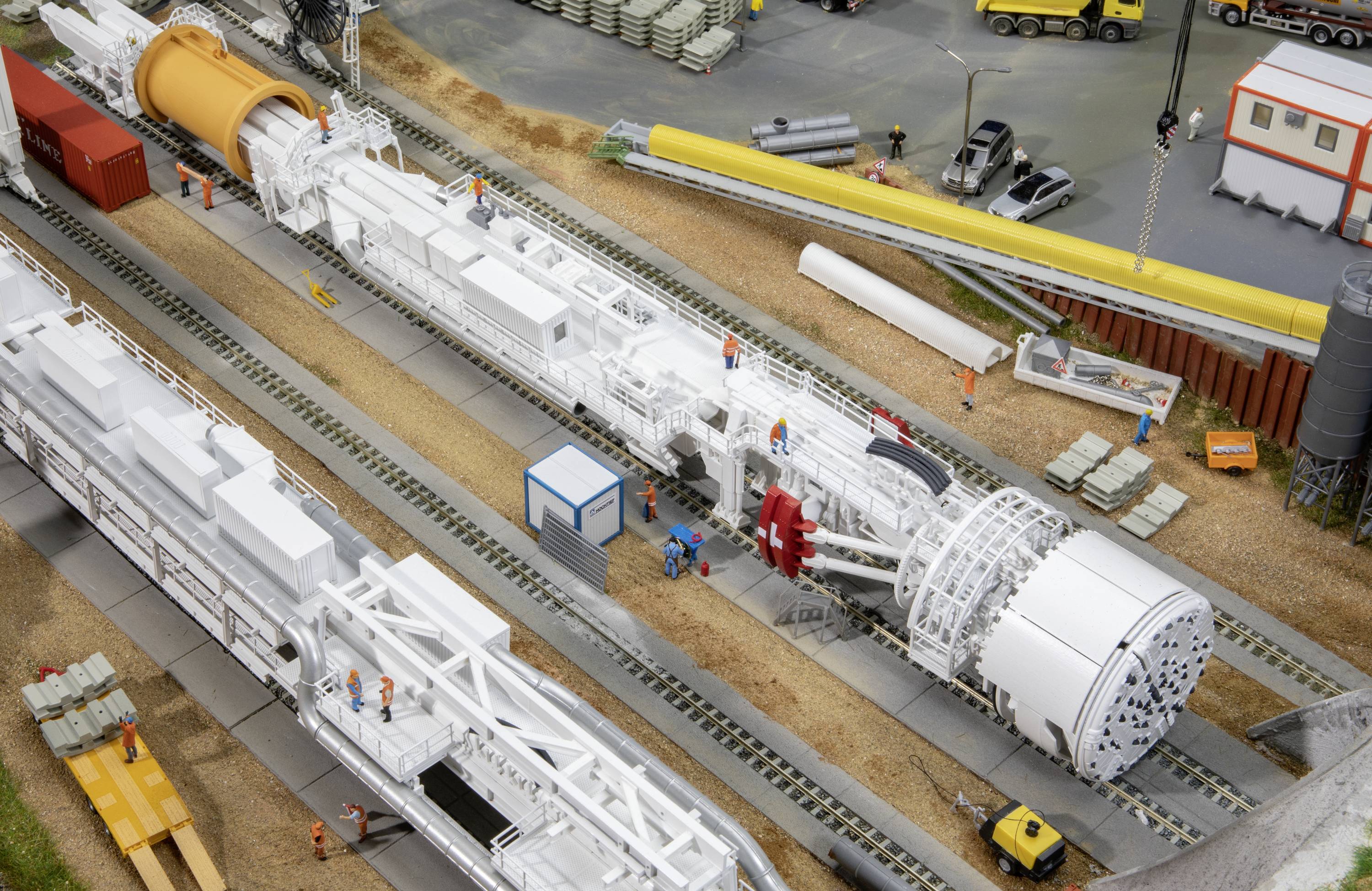 Model przedstawia plac budowy z dużą tarczą drążącą tunel, robotnikami i pojazdami budowlanymi. Umieszczony na szynach.