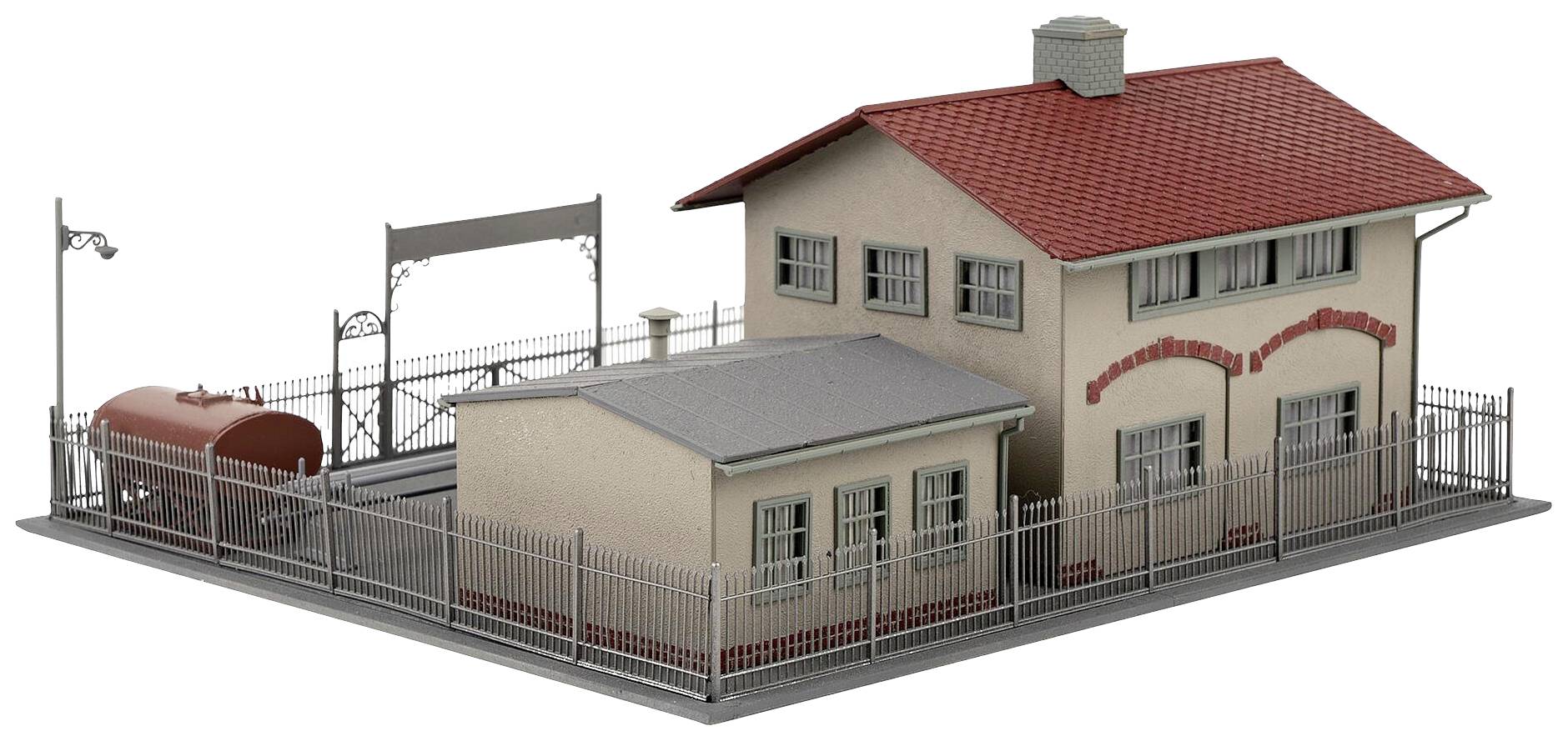 Model dwupiętrowego budynku z czerwonym dachem, otoczony płotem. Za nim znajduje się mniejsza dobudówka i duży zbiornik.