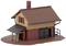 Mały domek modelowy z brązowym dachem i żółtą elewacją. Posiada czarne drzwi i czarny daszek nad wejściem.